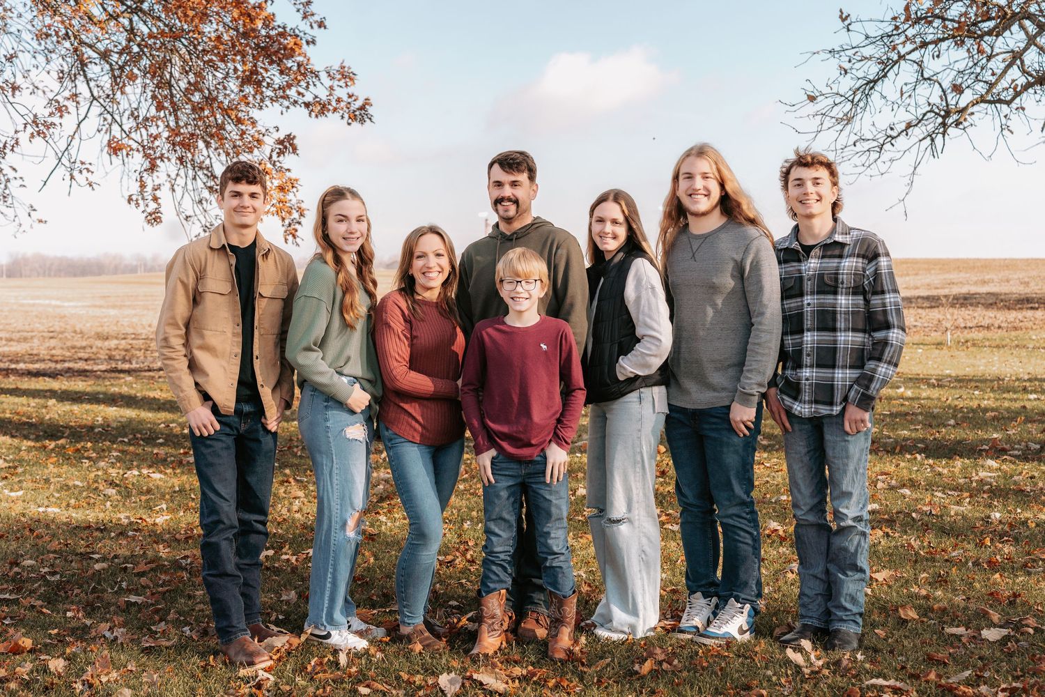 Panoramic group photo of people lined up outdoors against an autumn landscape backdrop.
