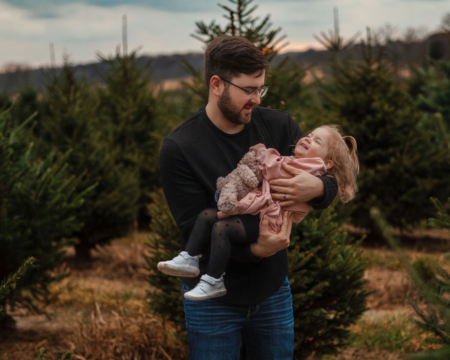 Couple shares intimate moments at a Christmas tree farm during winter.