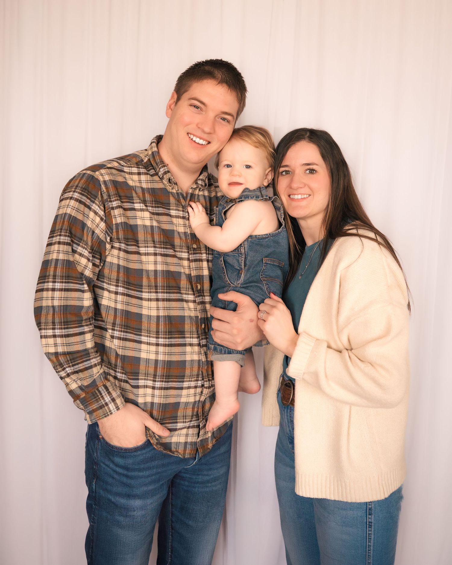A family poses together against a white background wearing casual fall clothing.