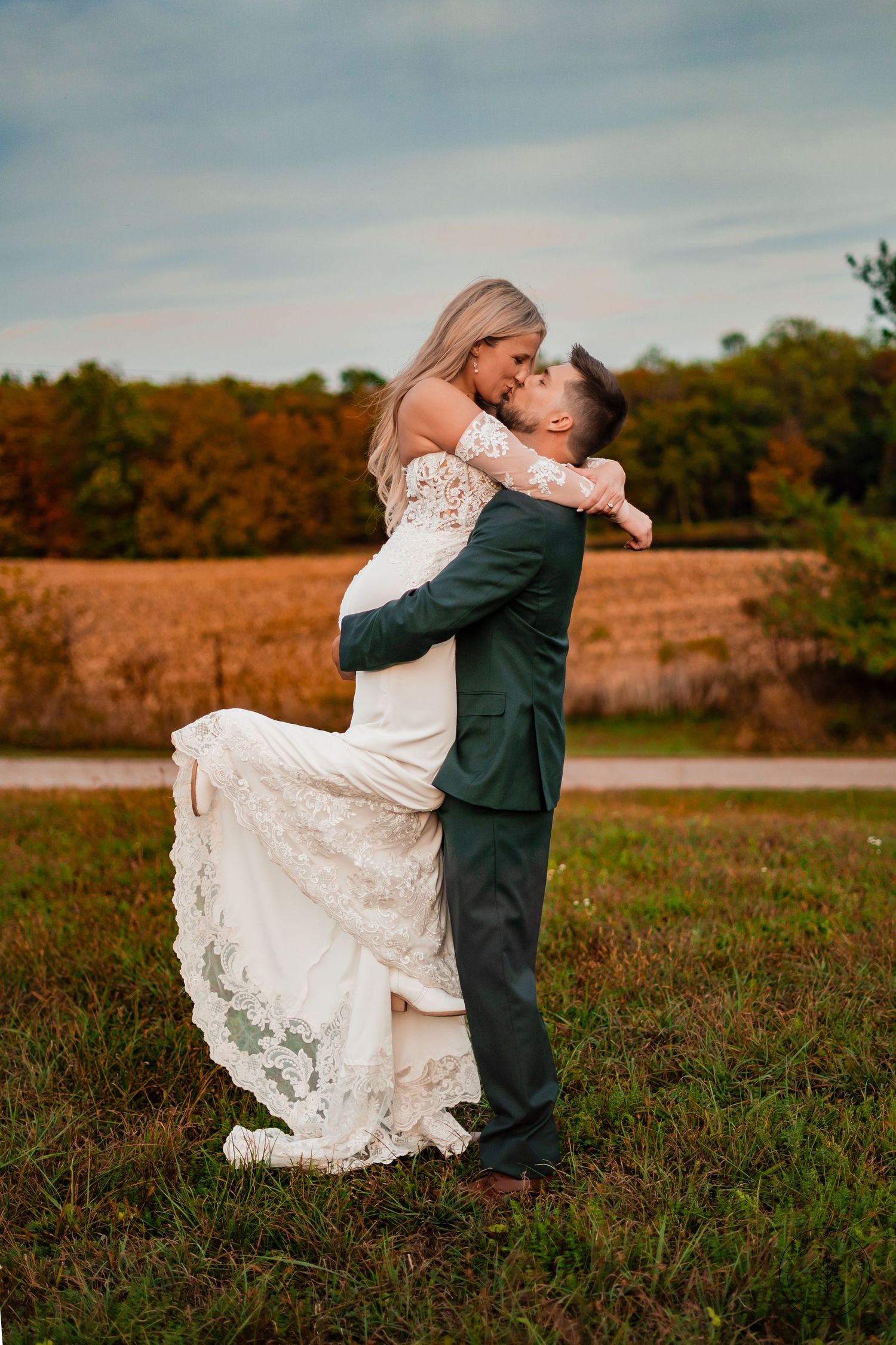 A couple in wedding attire embracing in a romantic spin against an autumn landscape.