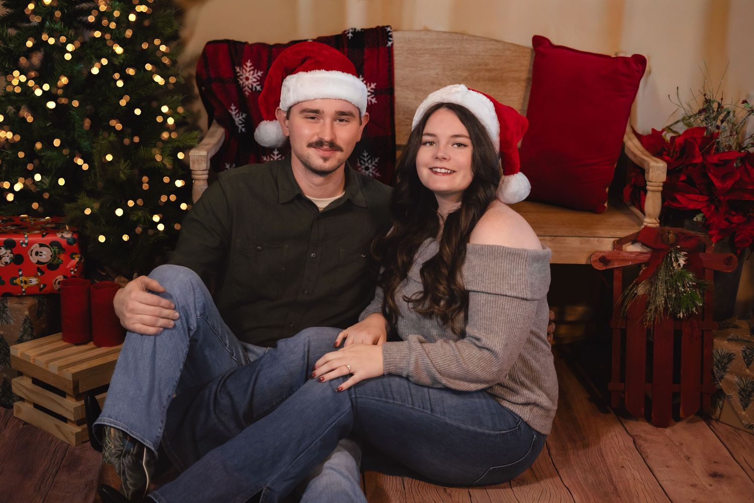 A cozy holiday scene with couple in Santa hats by Christmas tree.