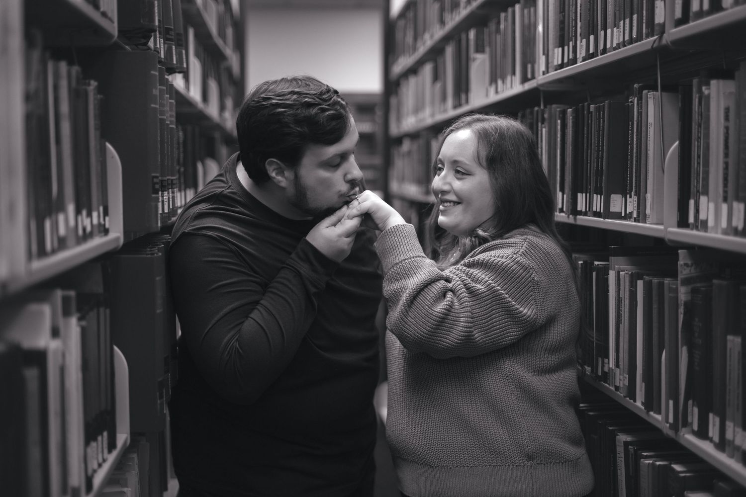 A couple sharing an intimate moment between library shelves in black and white.