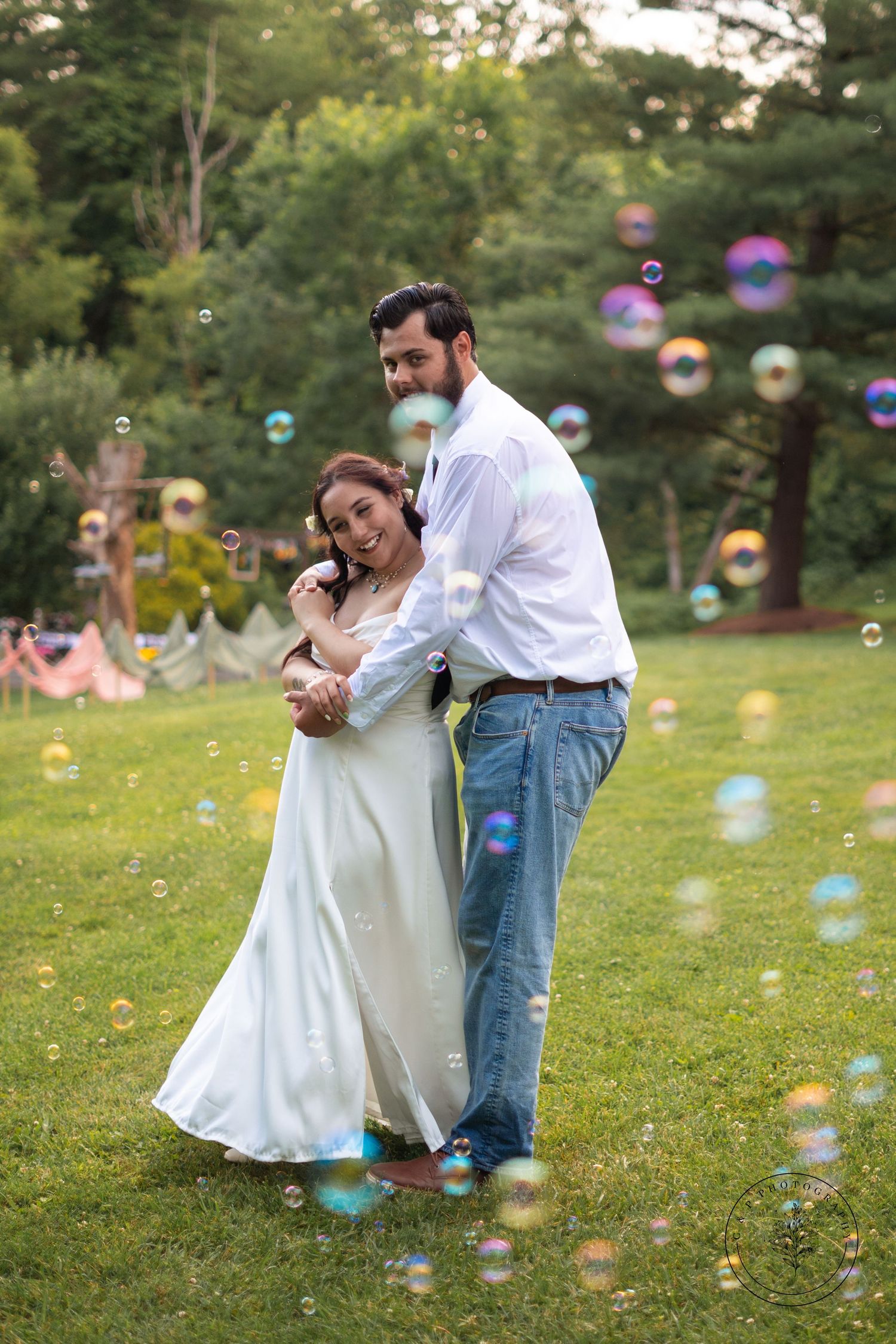 Couple dances amid floating soap bubbles in garden setting during wedding celebration.