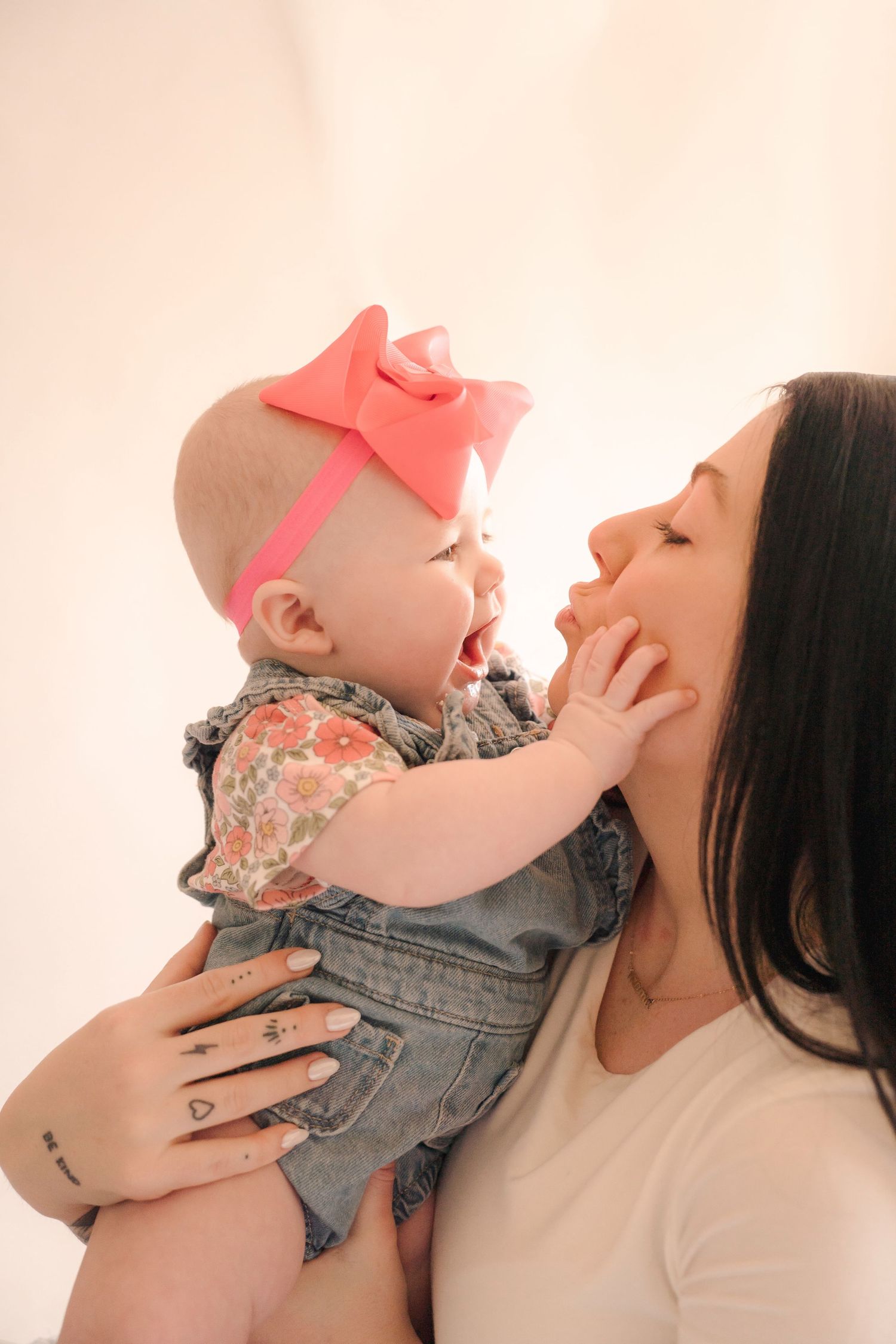 Mother and baby in matching denim share joyful interaction against white backdrop.