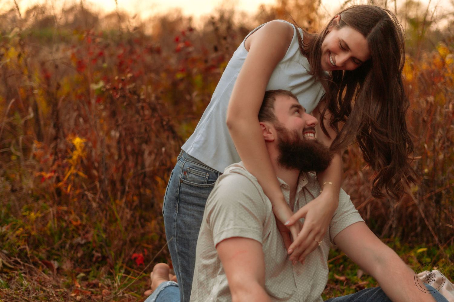 A playful couple sharing a candid moment during sunset in a field.