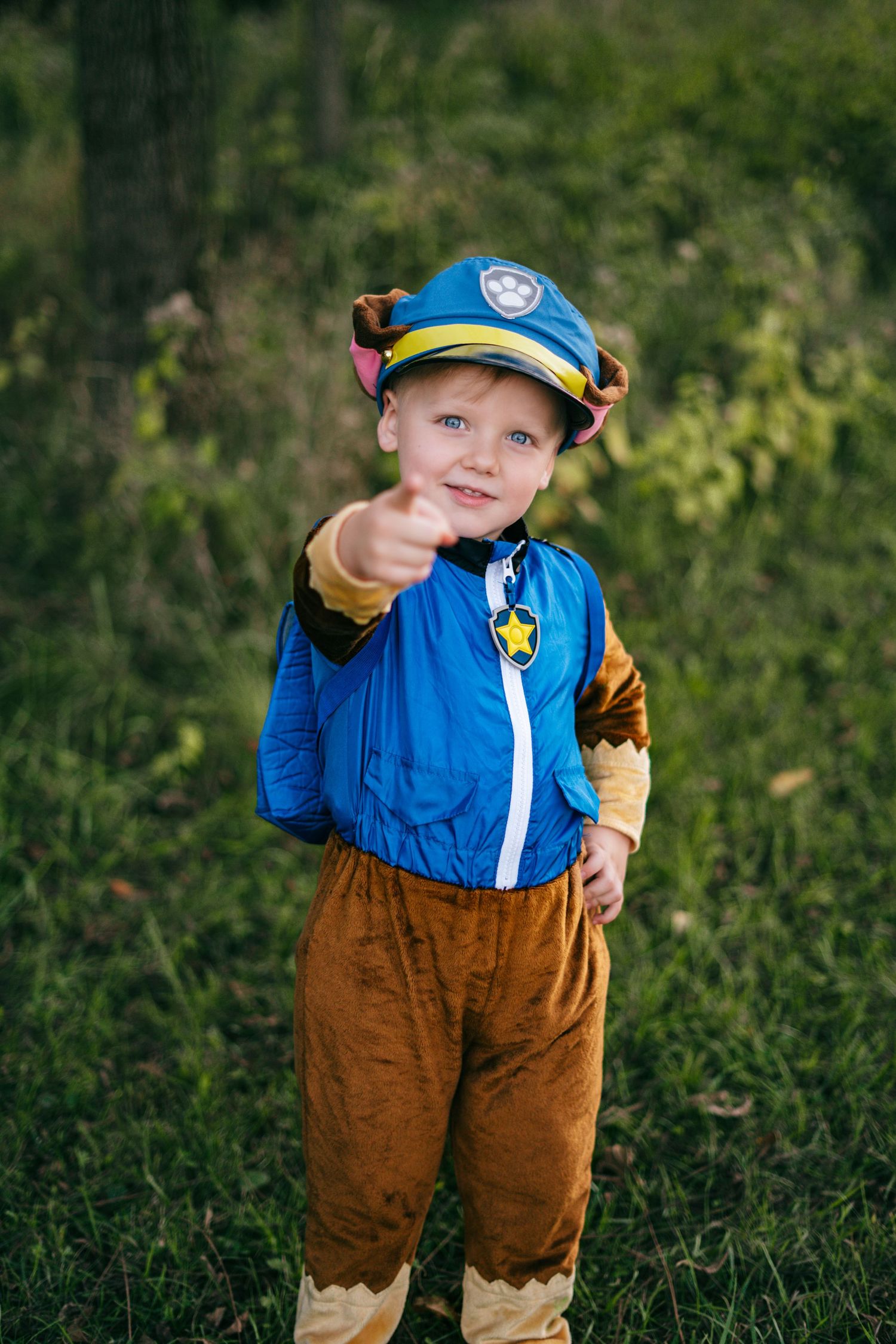 Child in blue and brown Paw Patrol Chase costume playing in outdoor setting.