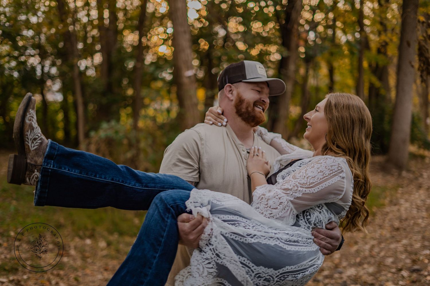 A romantic fall engagement photo of a couple embracing in the woods with warm sunset lighting.