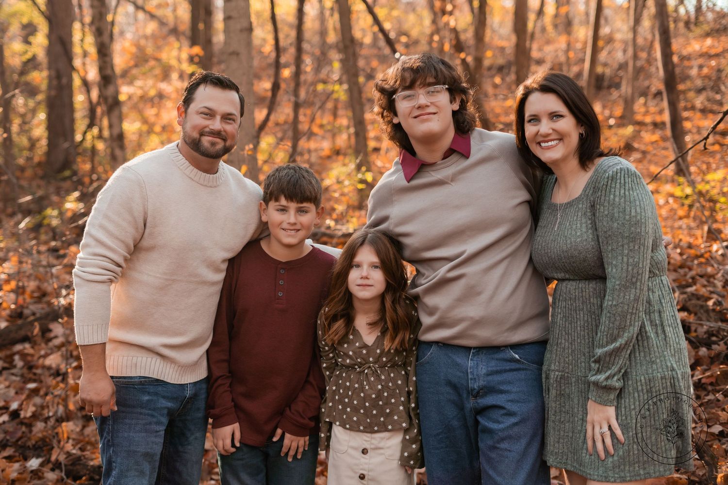 A warm autumn family portrait with five people in cozy sweaters among fallen leaves.