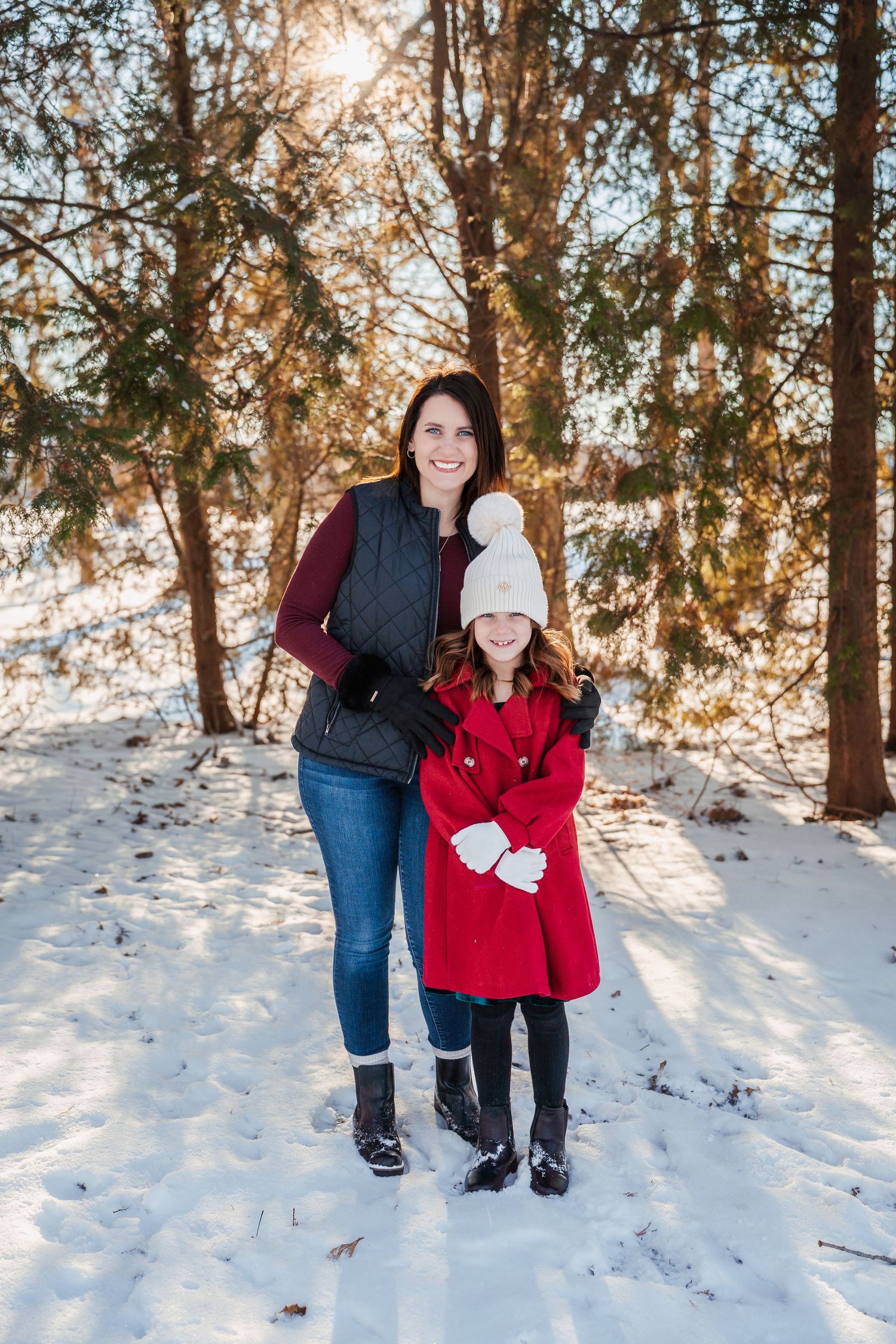 A winter scene with two people standing together on a snowy path surrounded by sunlit trees.