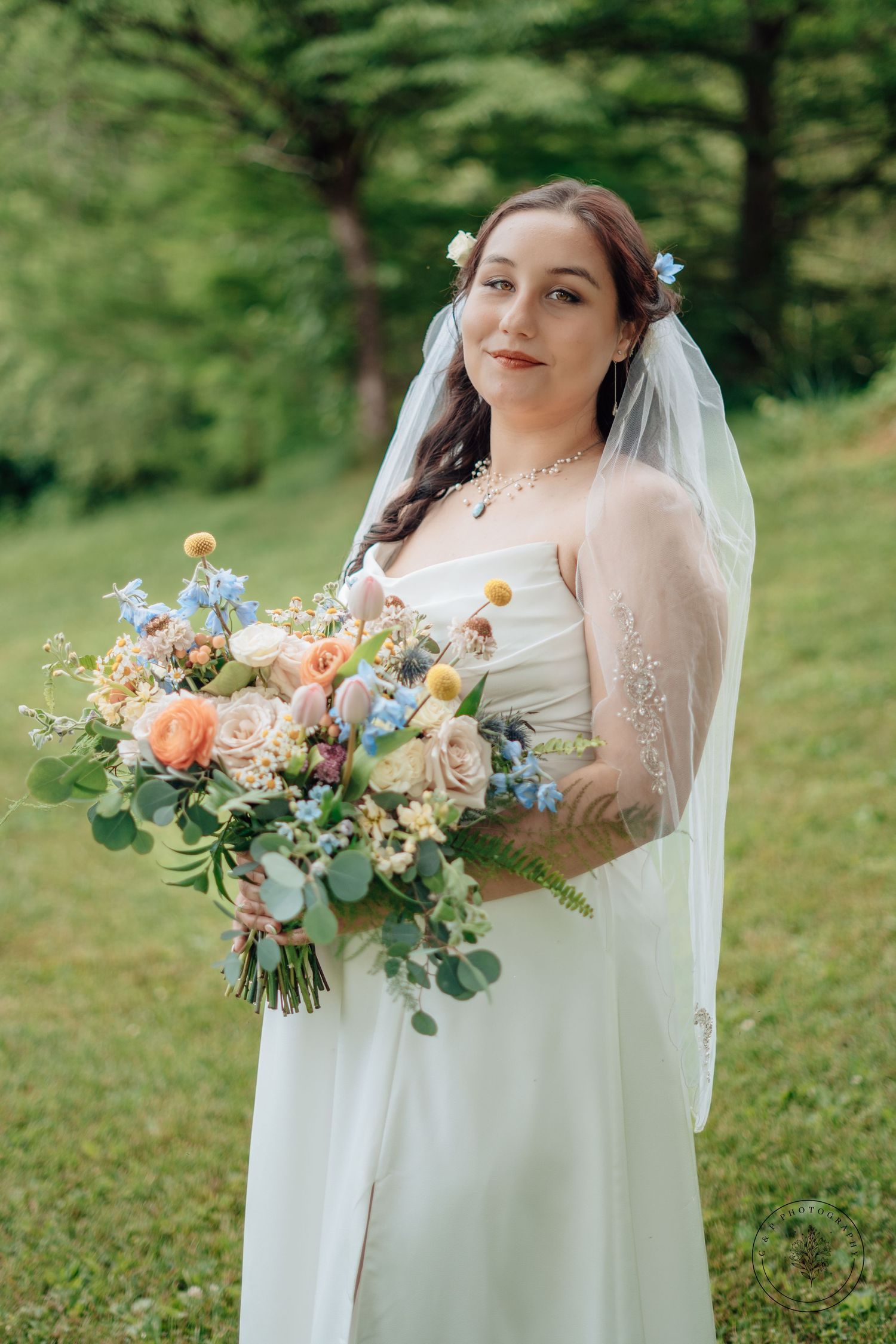 Spring bride in white dress holding colorful bouquet with blue and peach flowers.