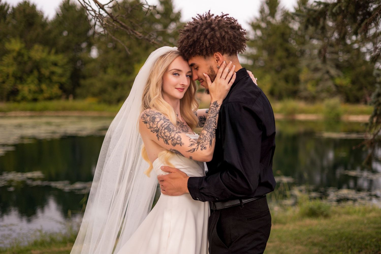 An emotional wedding moment between newlyweds by a pond.