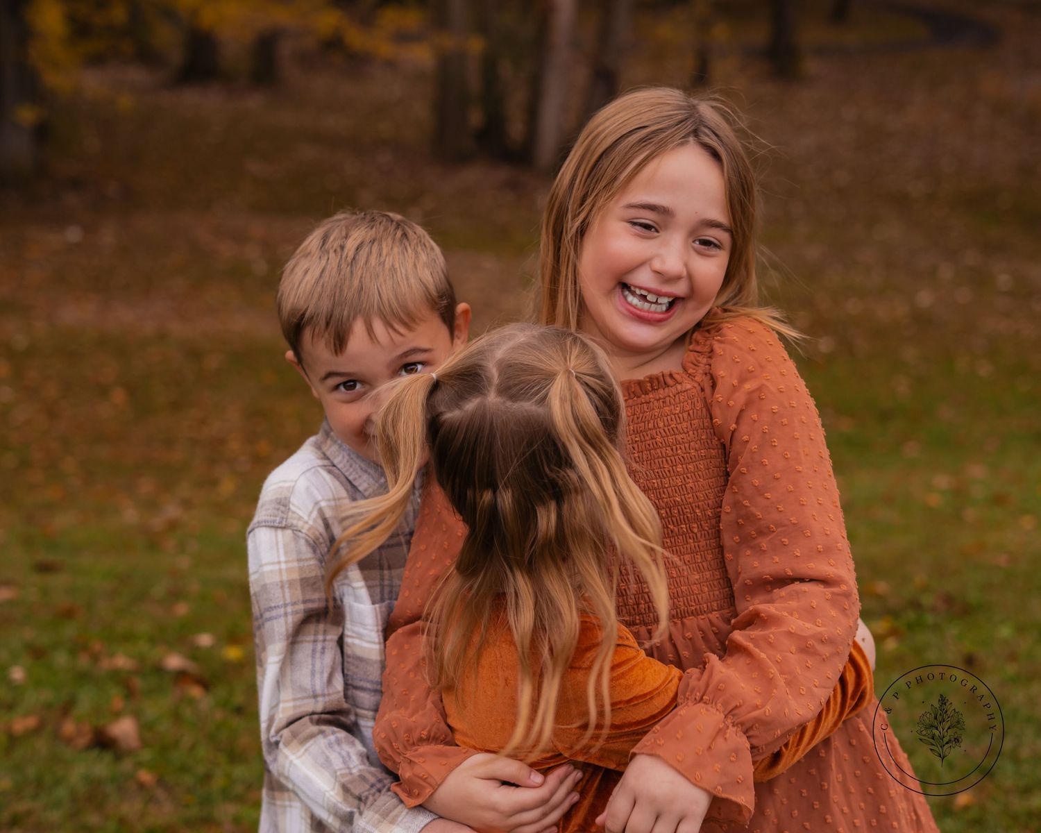 A joyful outdoor autumn photoshoot with people embracing and laughing together in warm orange sweaters.
