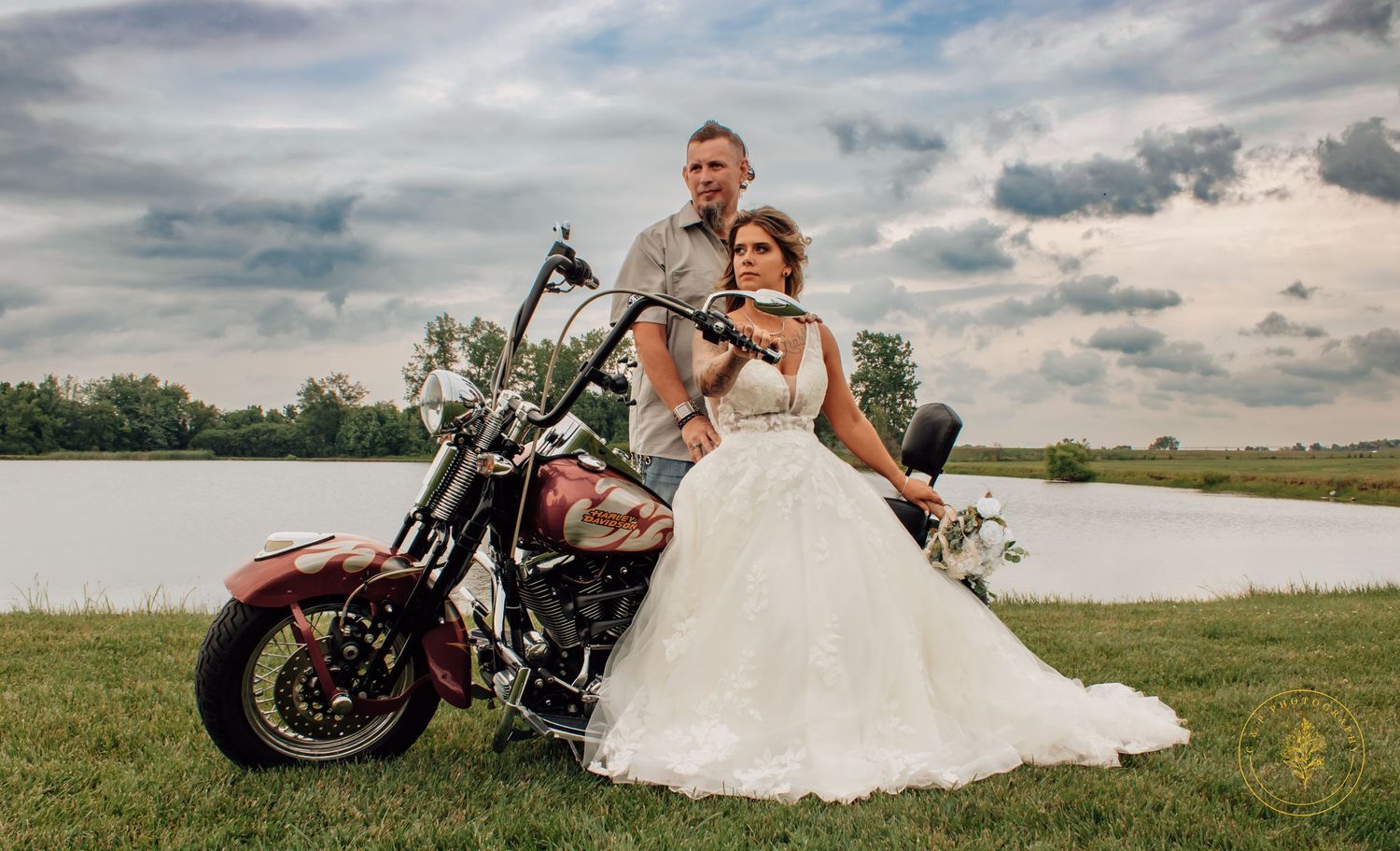 A couple poses with a motorcycle in a scenic outdoor wedding photo shoot.