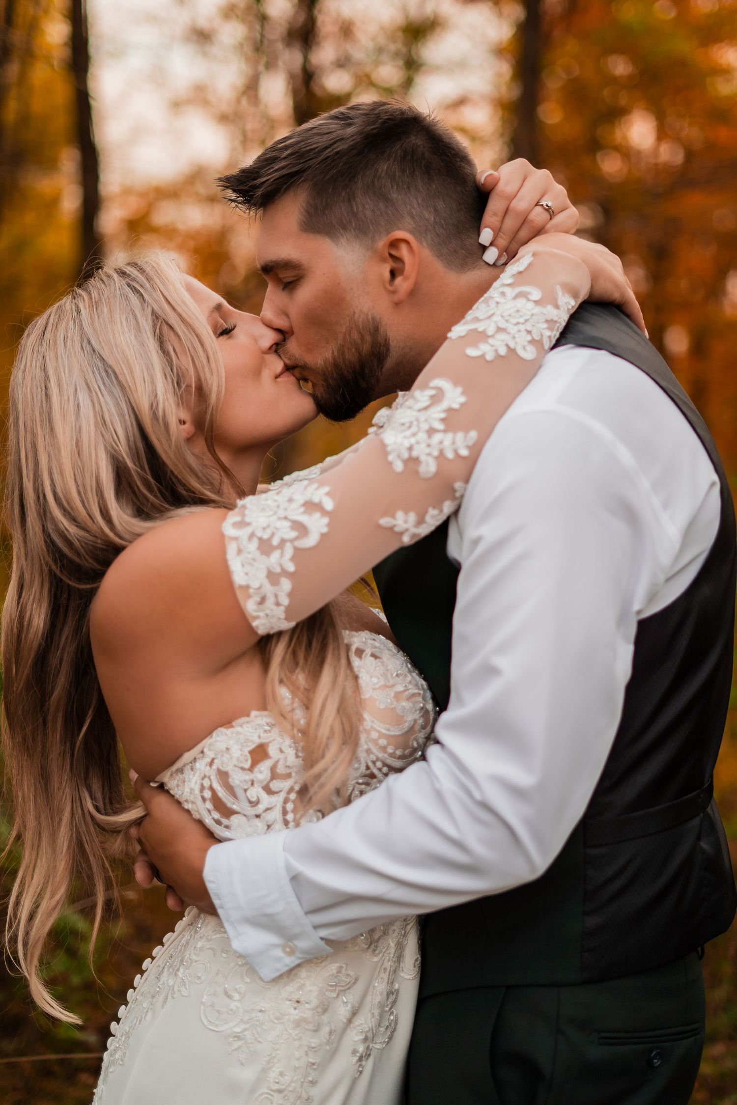 Romantic wedding couple embracing in autumn forest setting.