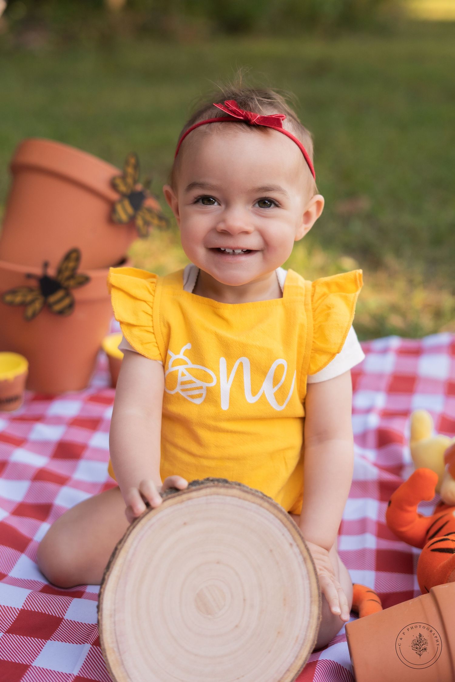 A toddler in a yellow ruffled outfit smiling during an autumn-themed picnic setup.