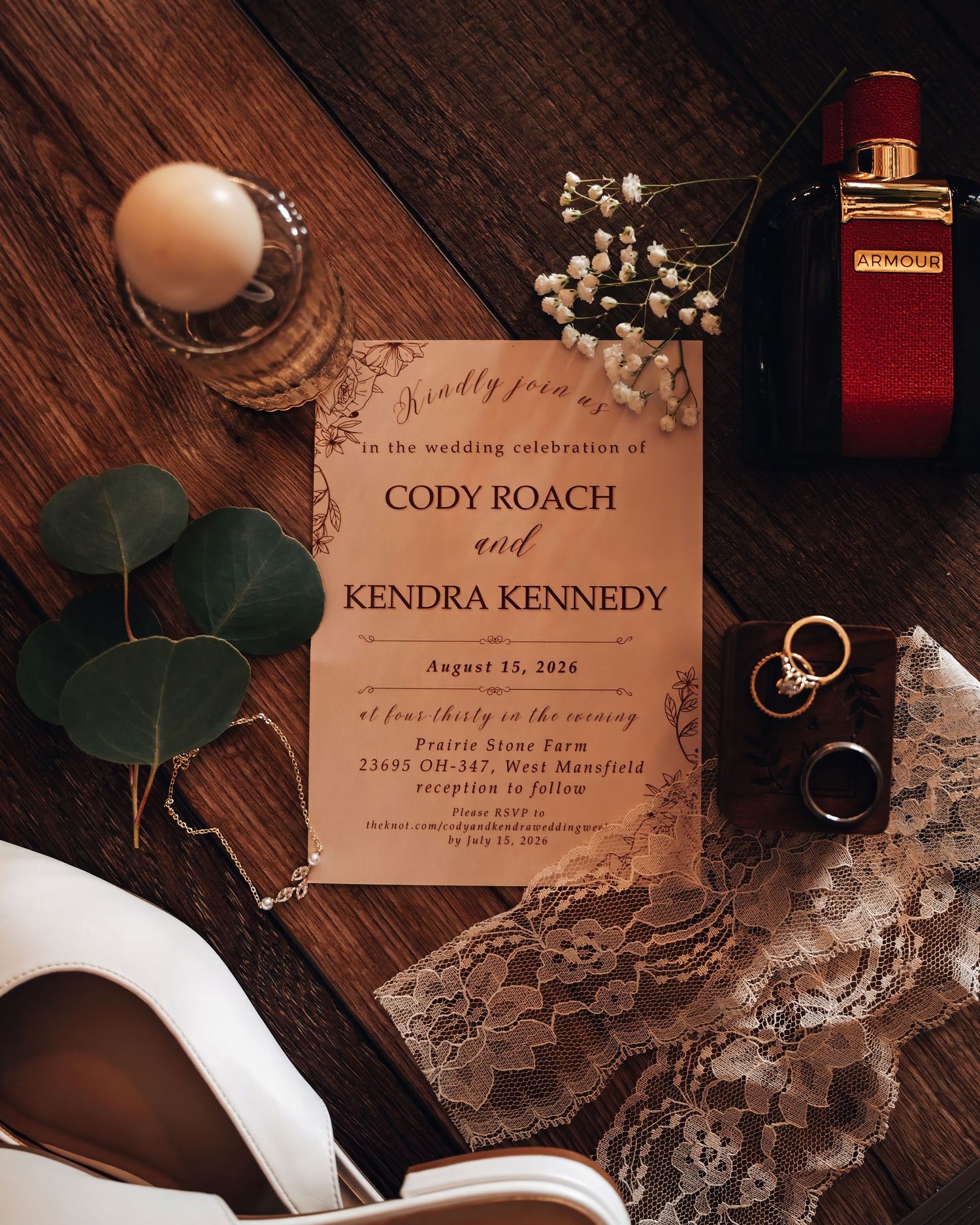 Elegant wedding invitation for Cody Roach and Kendra Kennedy on a rustic wood surface with rings, lace, and floral accents.