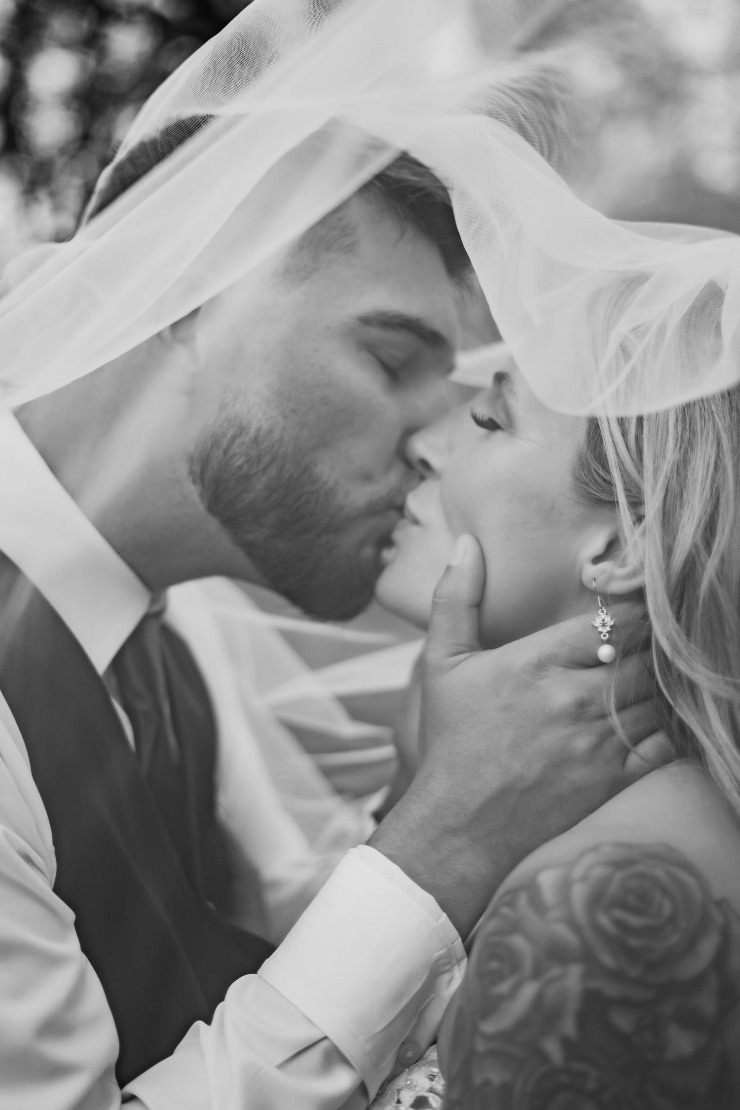 A black and white intimate wedding portrait under a flowing veil.