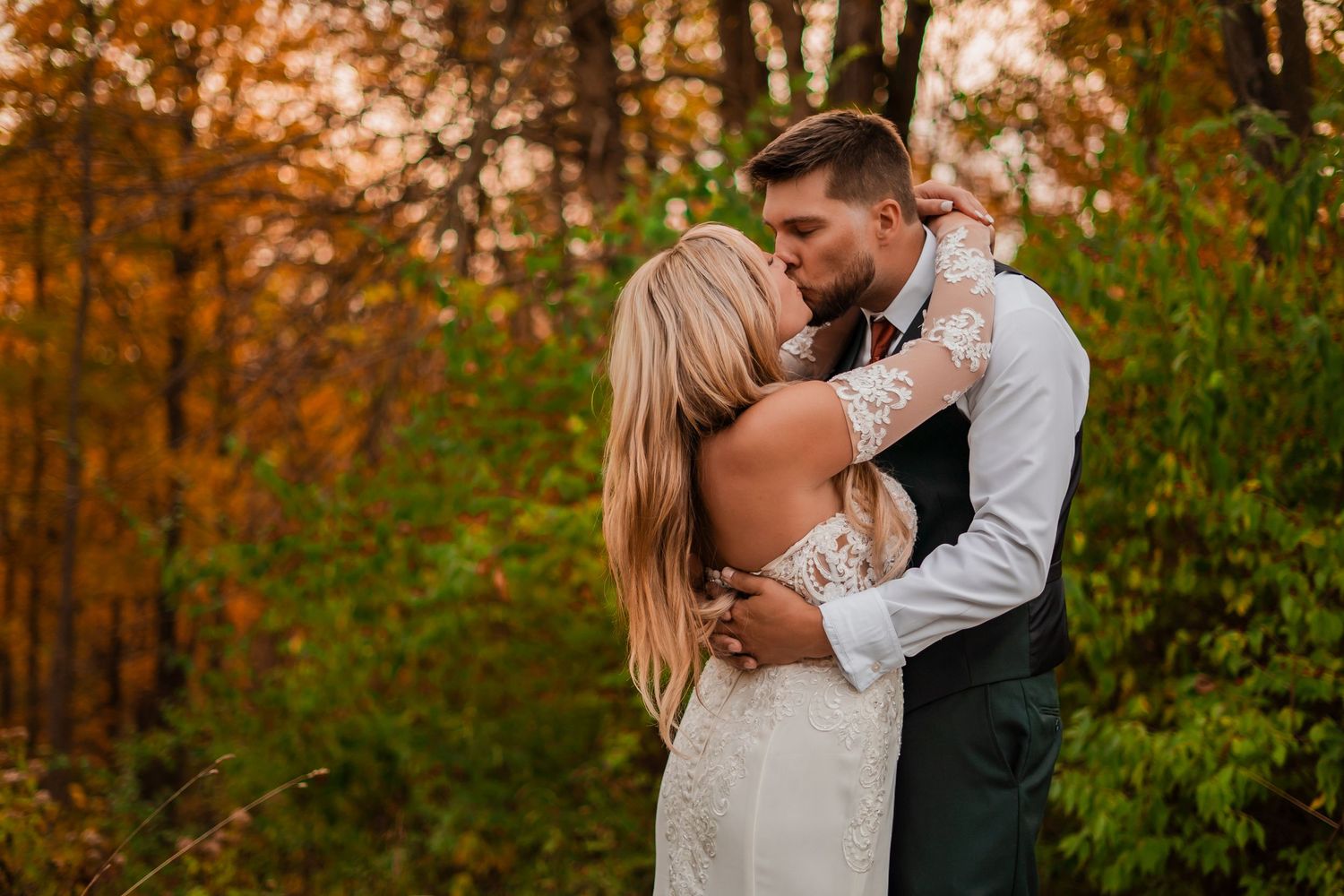 A romantic embrace between newlyweds in a forest with autumn foliage creating a warm backdrop.