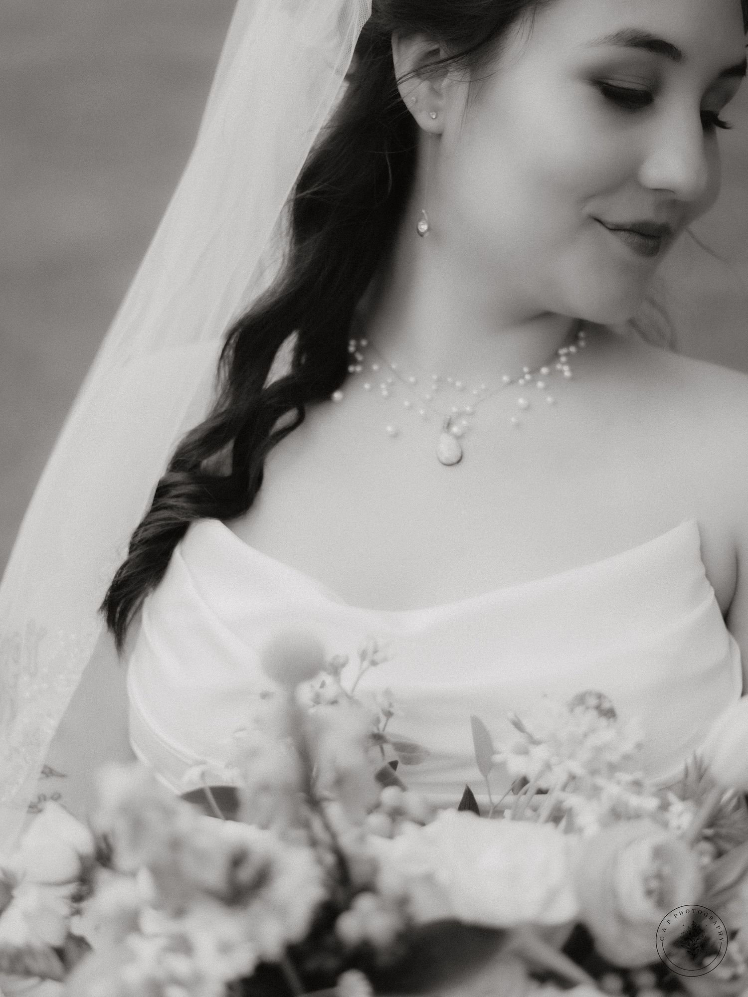 A black and white bridal portrait featuring delicate pearl jewelry and a classic white gown.