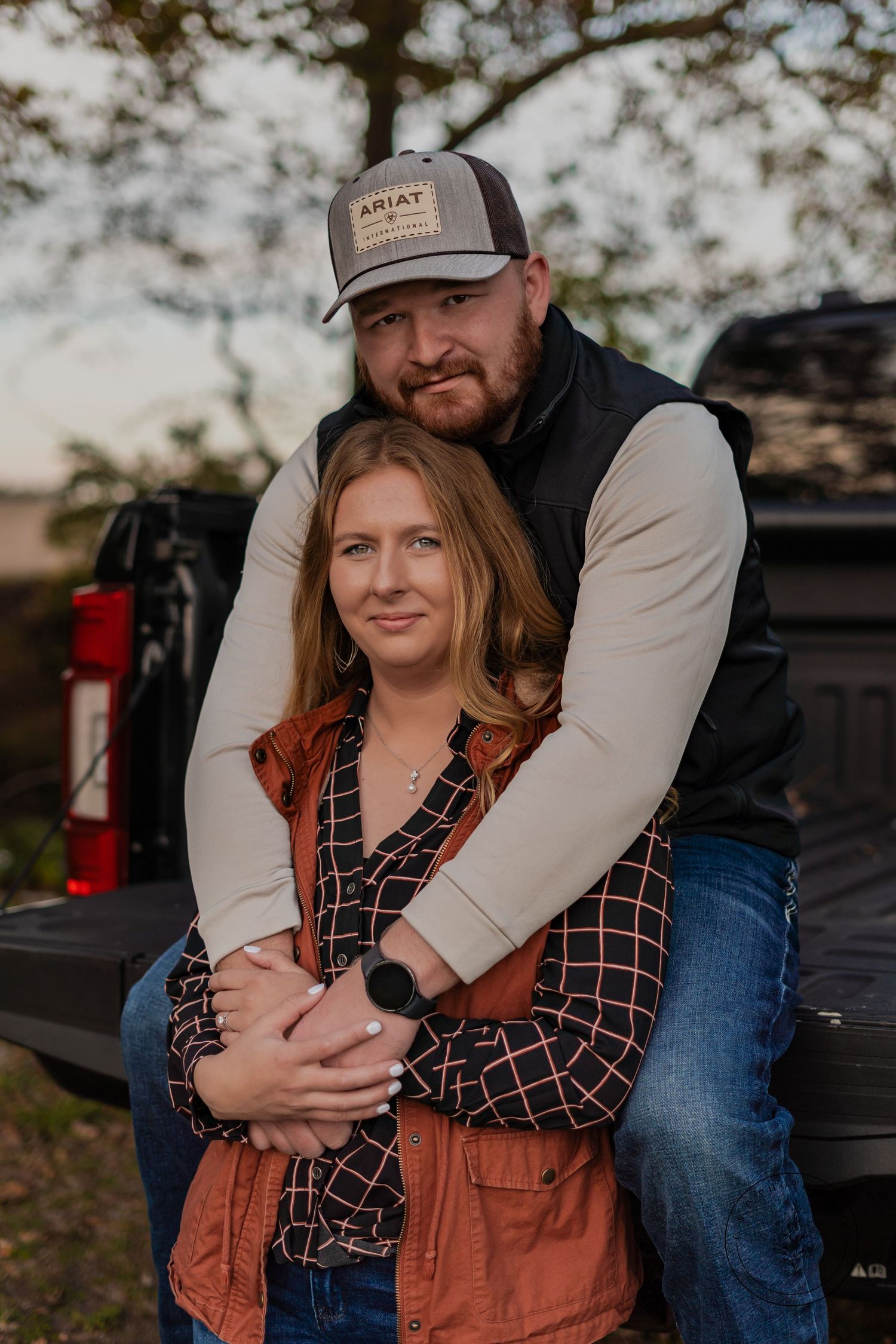 Couple embraces in casual fall attire while standing in front of a pickup truck at sunset.