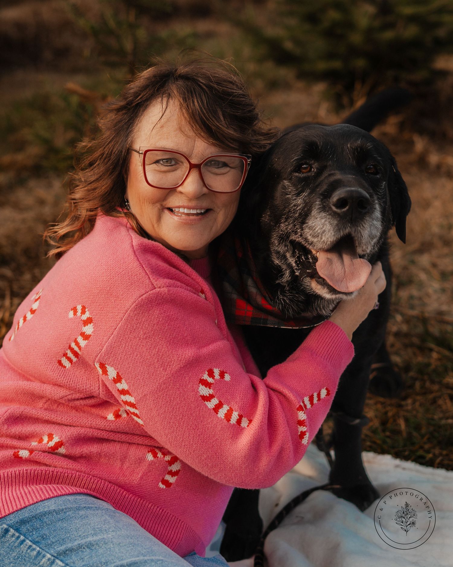 Person in pink sweater cuddling with black dog outdoors during autumn.