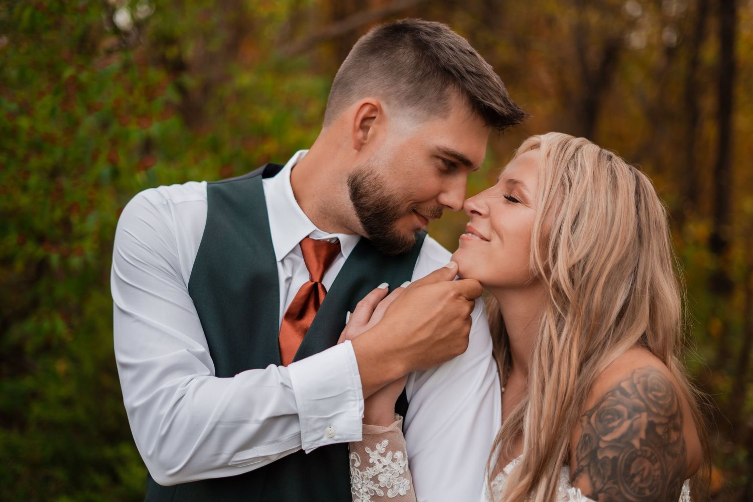 A romantic wedding moment captured between a couple in front of fall foliage.