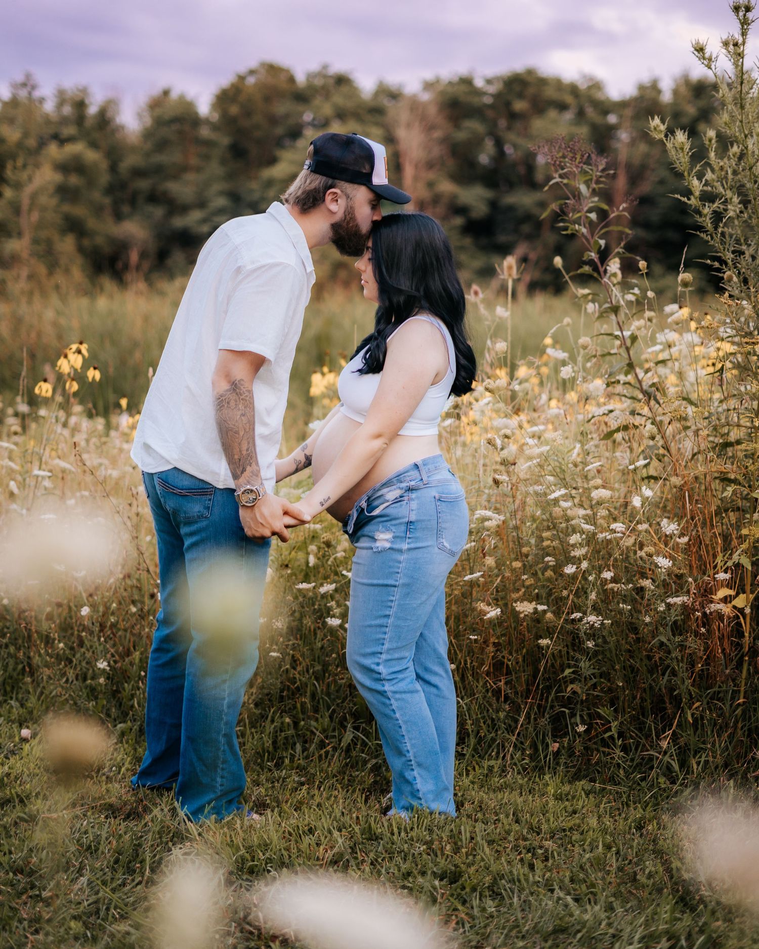 Couple shares intimate moment in wildflower meadow during golden hour sunset.