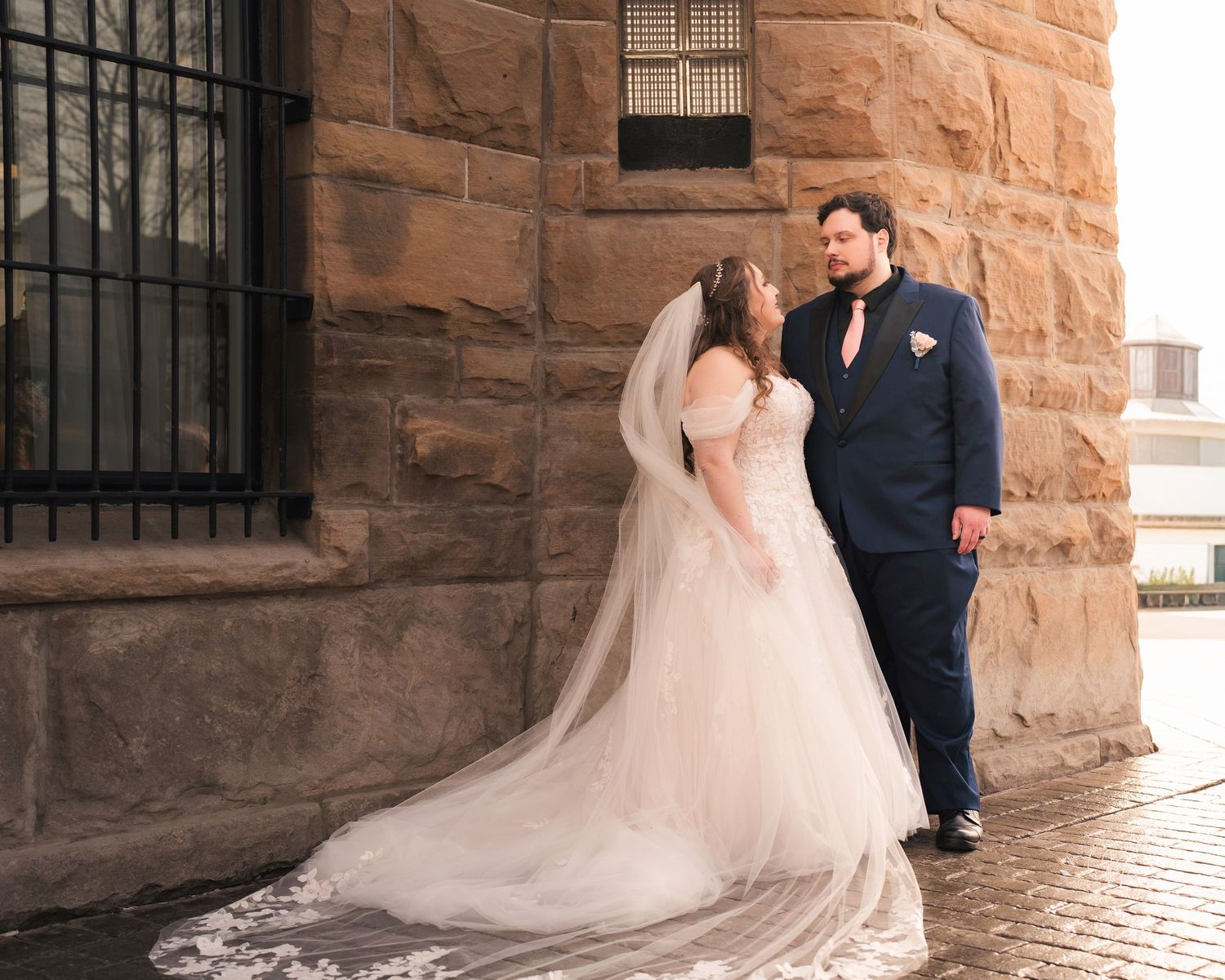 Wedding couple posing against stone wall with flowing white dress train.
