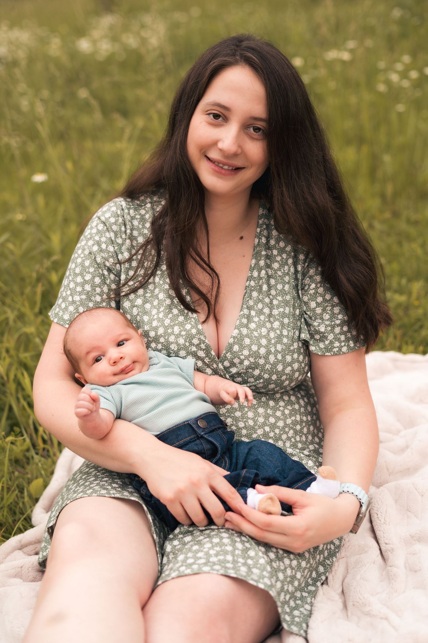 A tender moment between parent and baby sitting on blanket in summer meadow.