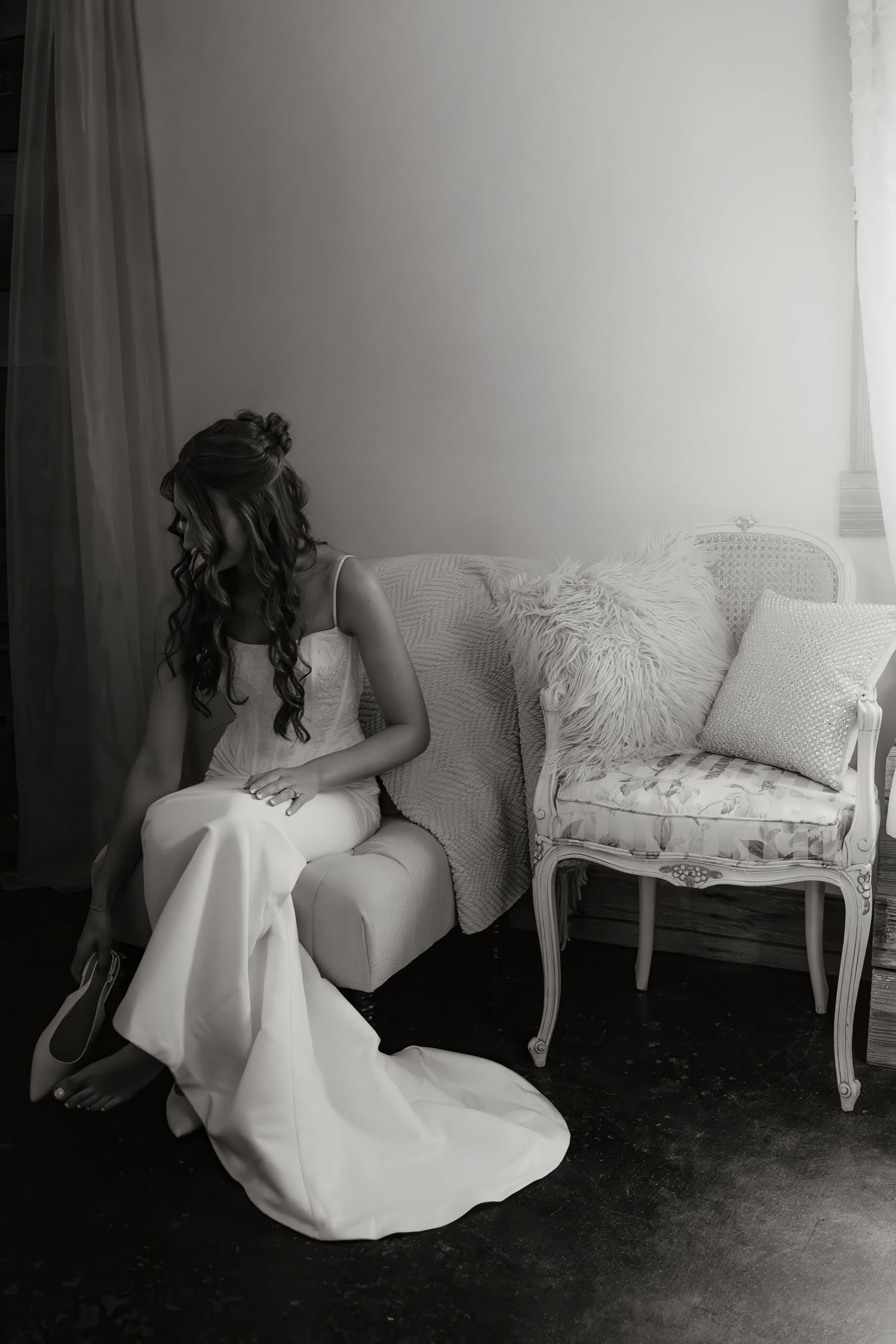 Black and white photo of a bride in a wedding gown sitting on an elegant vintage sofa, head bowed.