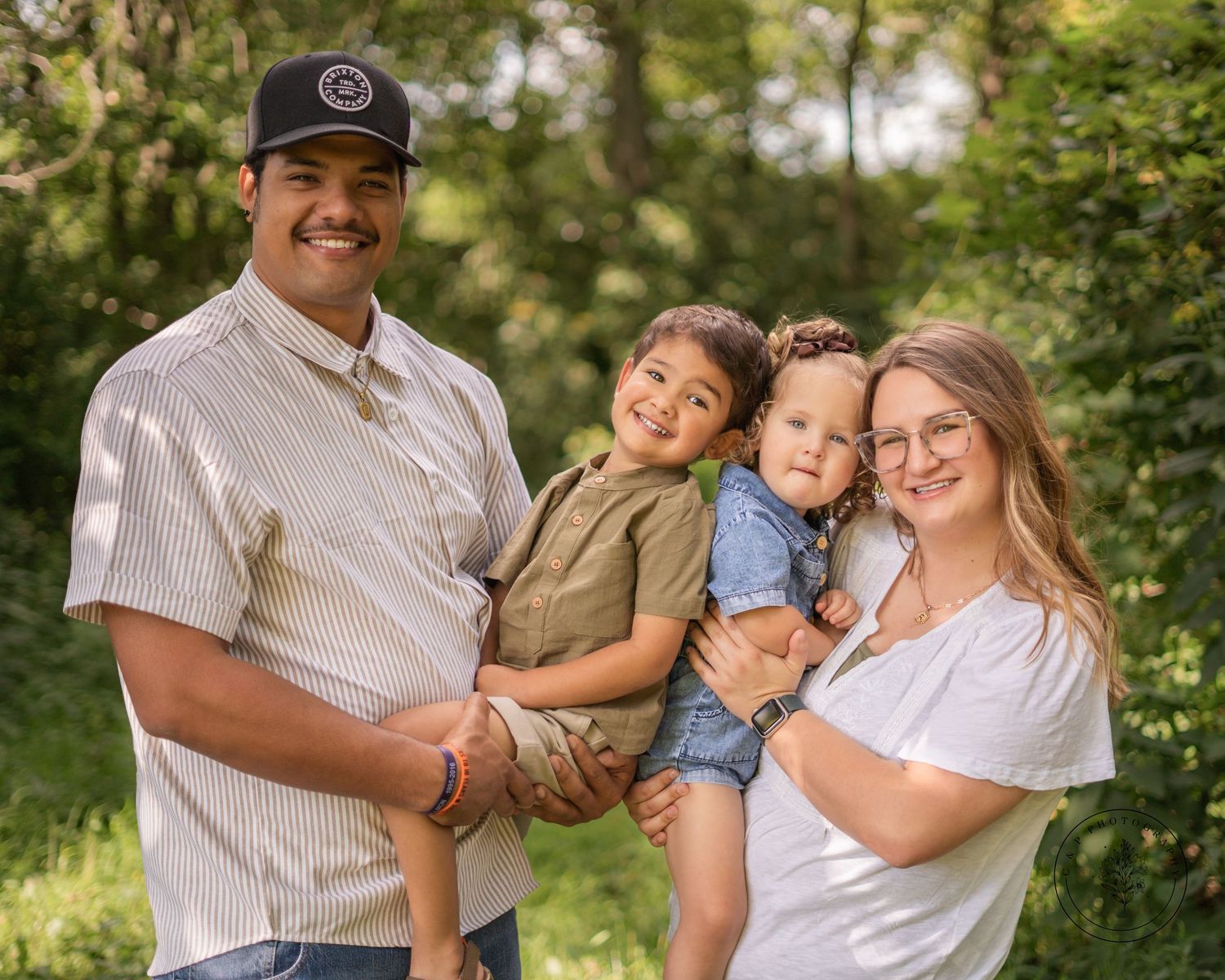 An outdoor summer portrait of a family of four against a green natural background.