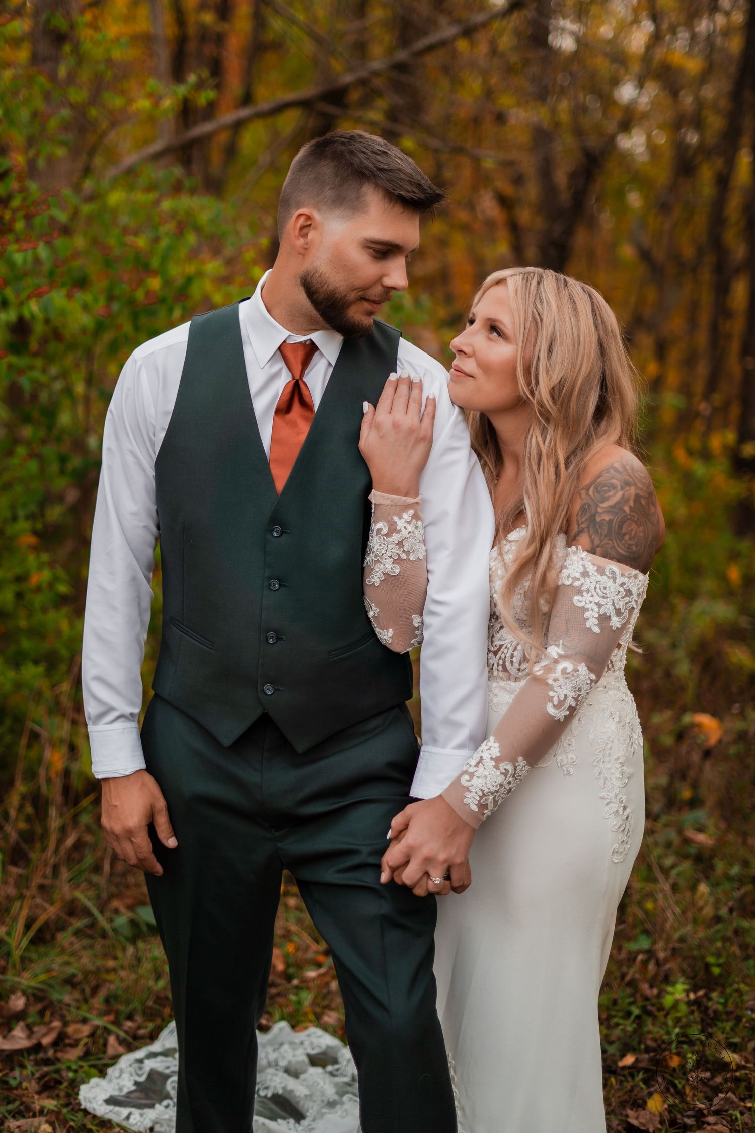 A couple in wedding attire sharing a romantic moment among autumn foliage.