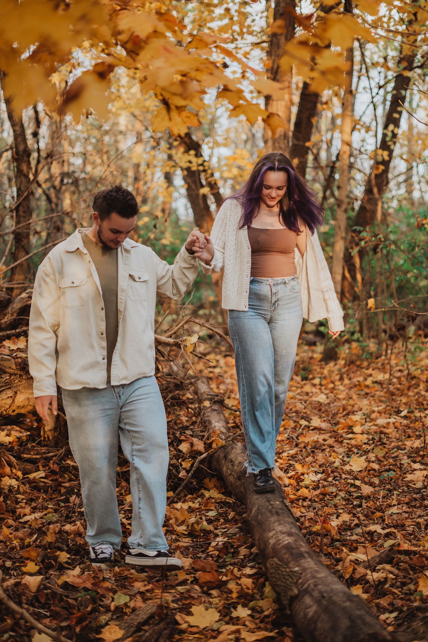 Couple walking through autumn forest with fallen leaves in casual attire.