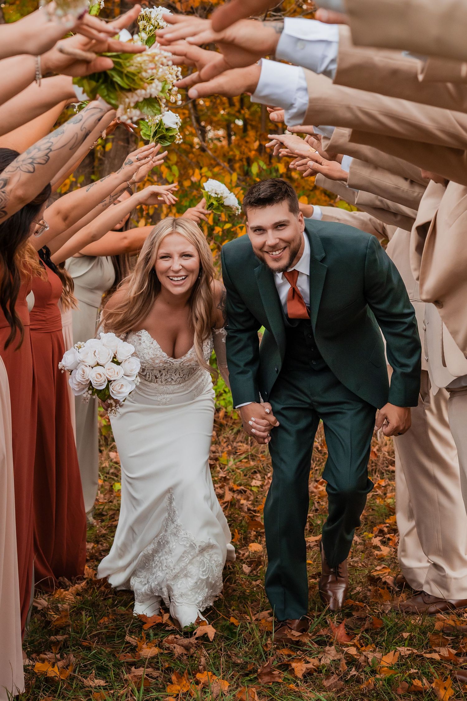 Wedding party poses playfully in autumn foliage with bridesmaids in rust-colored dresses.