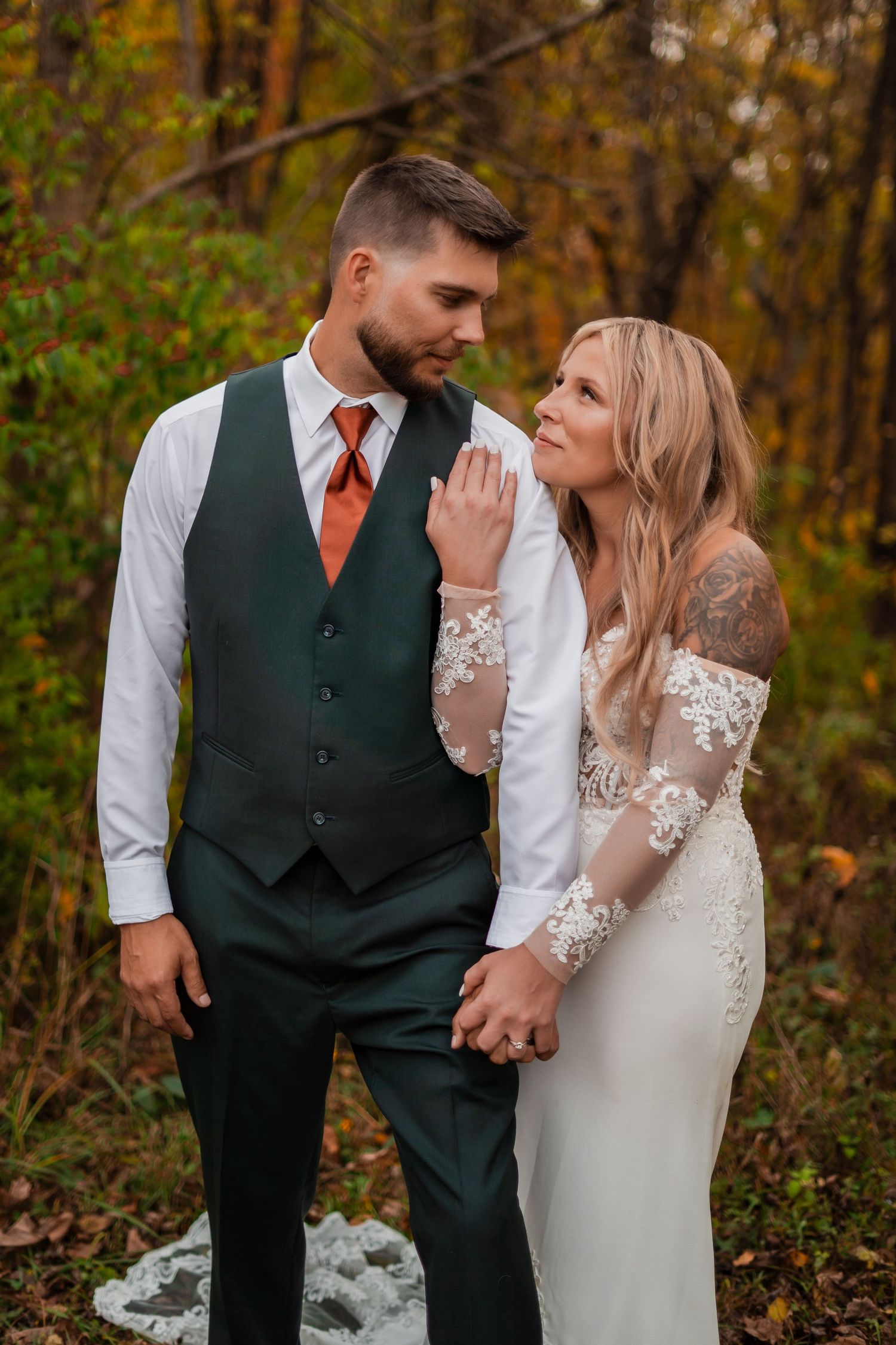 Wedding couple in elegant attire poses together against autumn foliage.