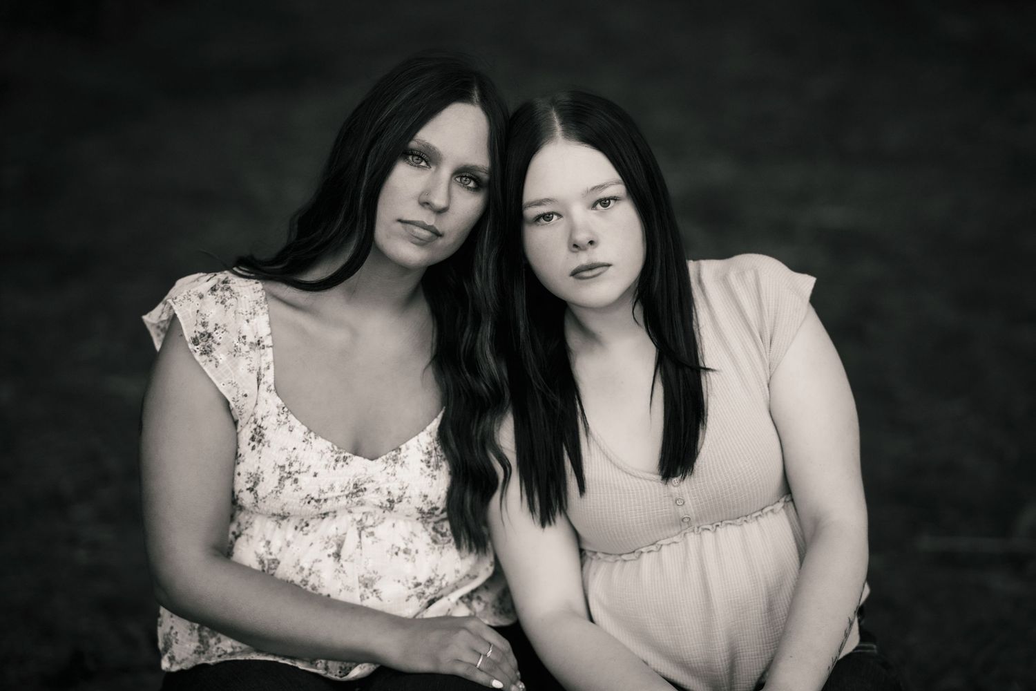 Black and white portrait of two dark-haired women sitting closely together outdoors.