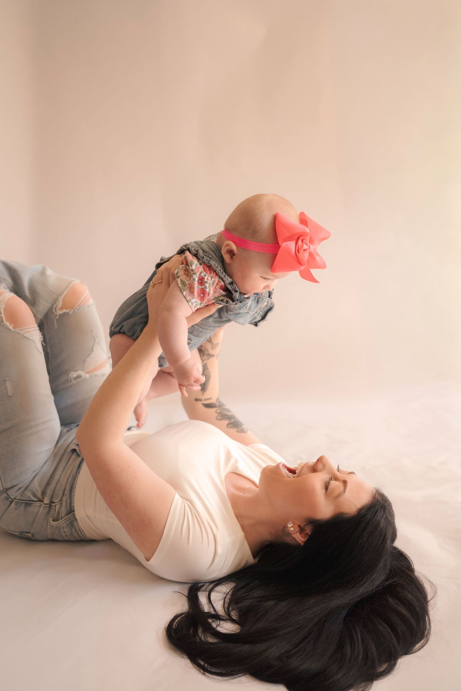 Maternity studio photo with woman in cream dress laying on light background.