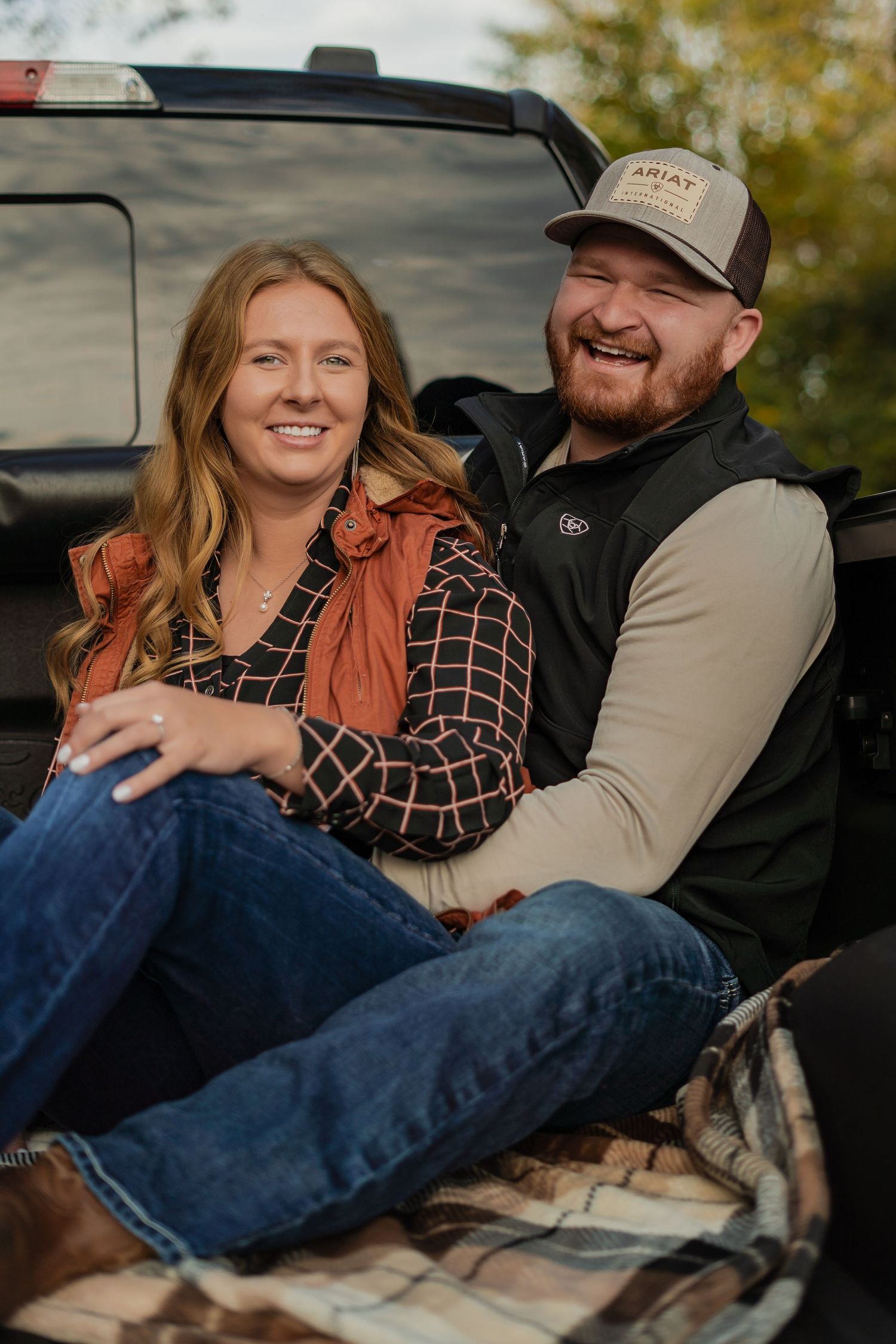 A couple sitting together in the bed of a pickup truck on an autumn day.