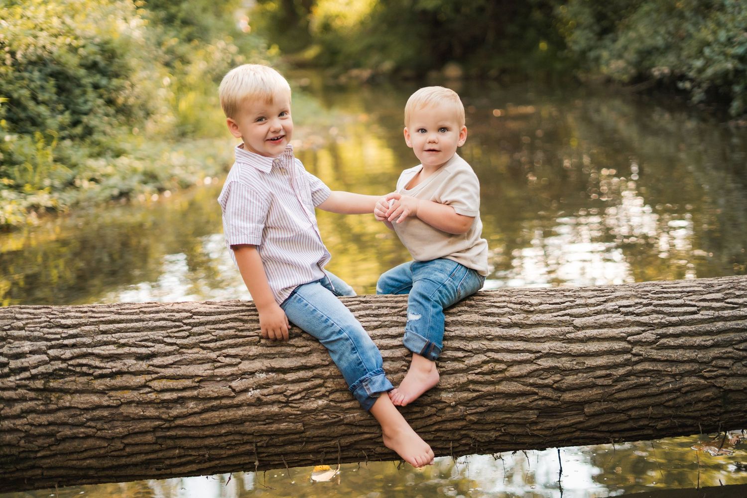Young children sit on a fallen log by a pond during golden hour.