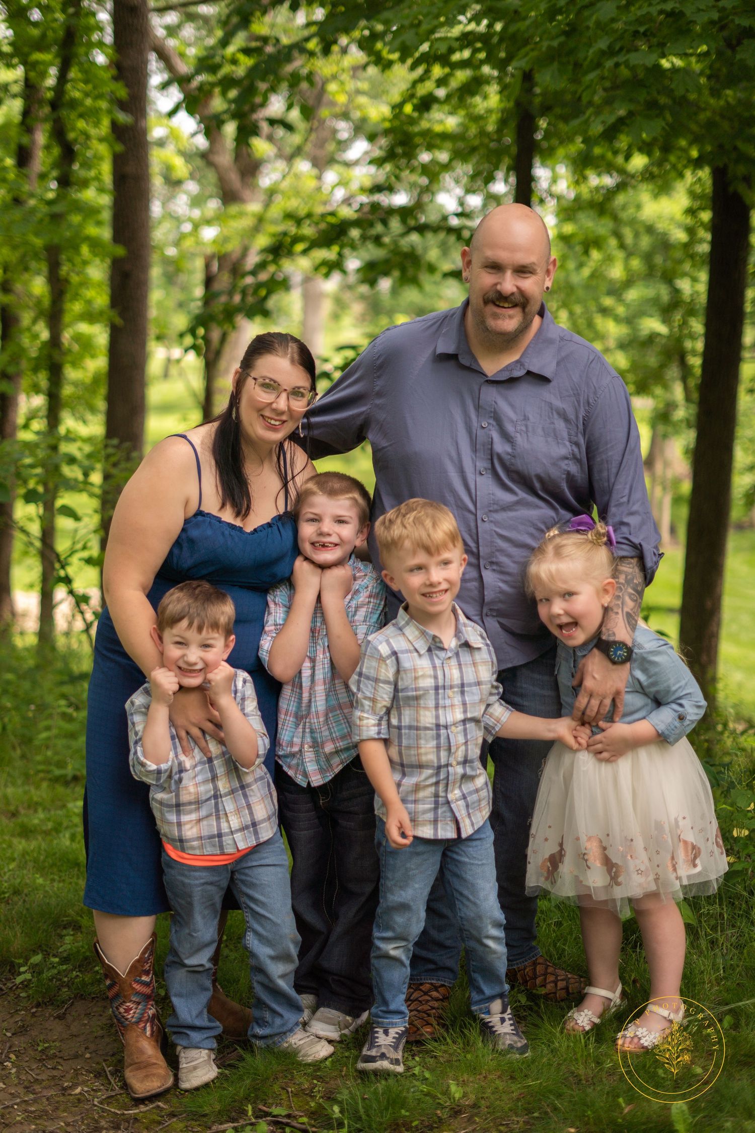 A family of six poses together on a wooded path wearing coordinated blue and casual outfits.