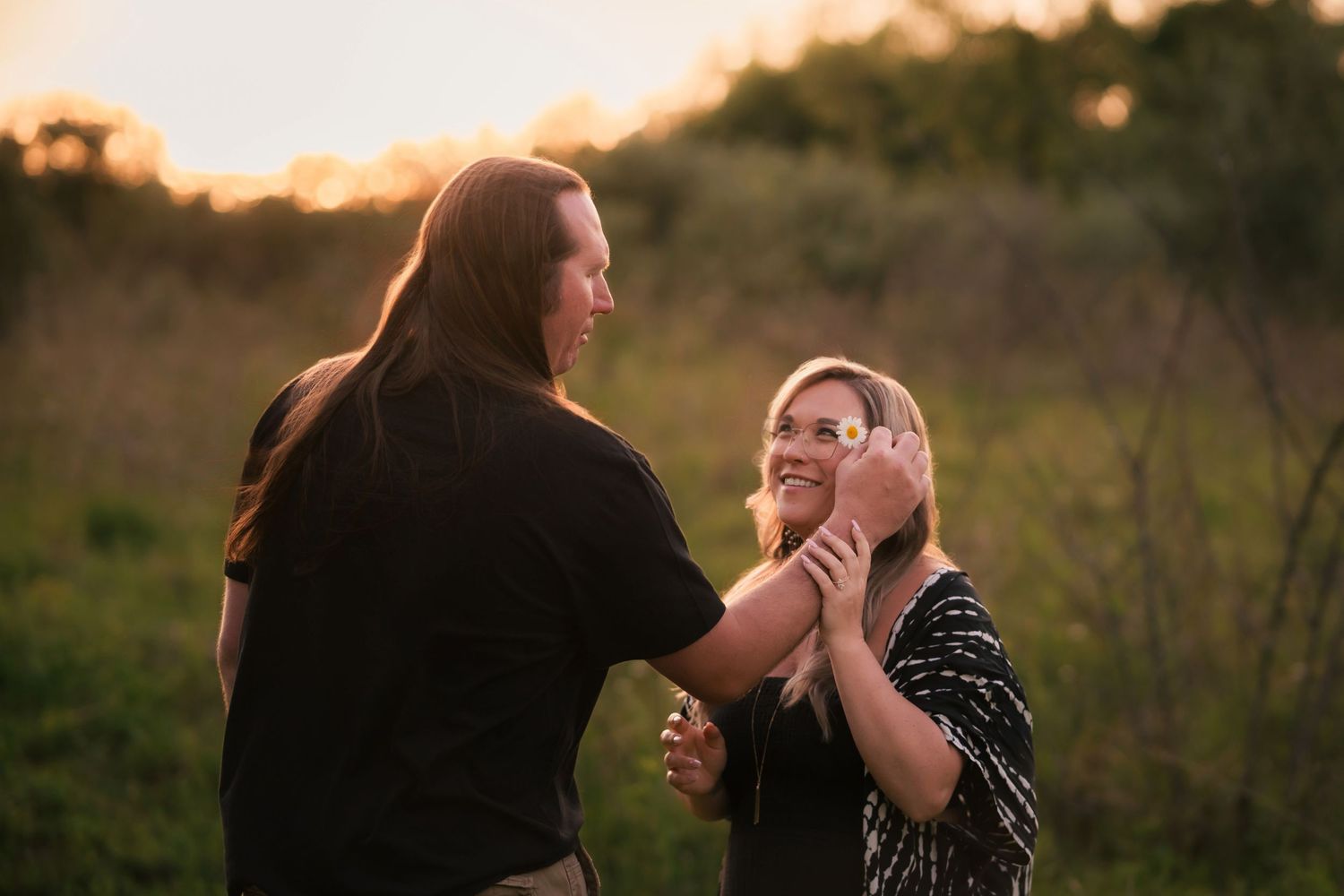 Couple sharing a tender moment in a sunlit field at golden hour, smiling together.