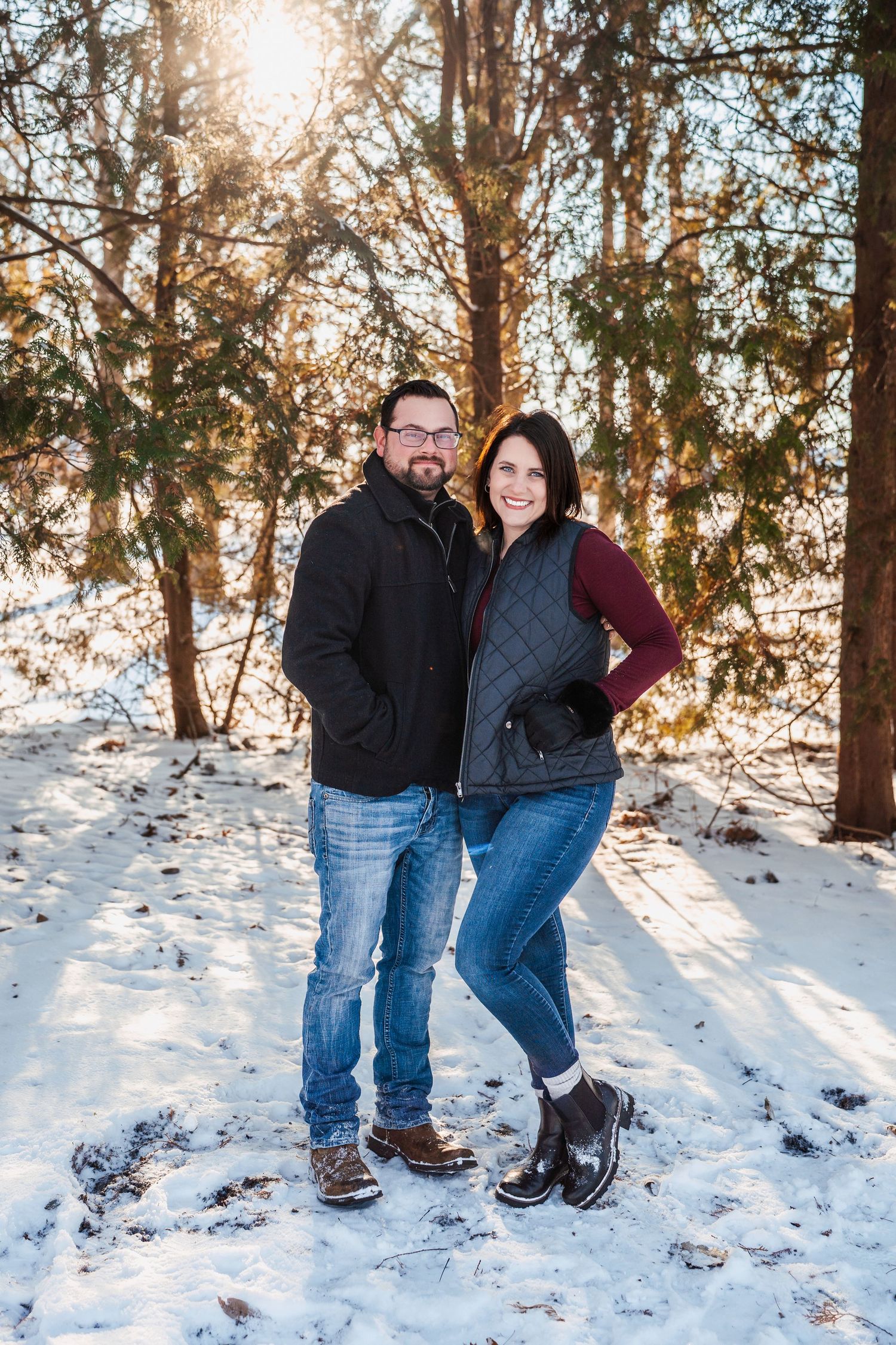 Couple poses together in snowy winter forest setting.