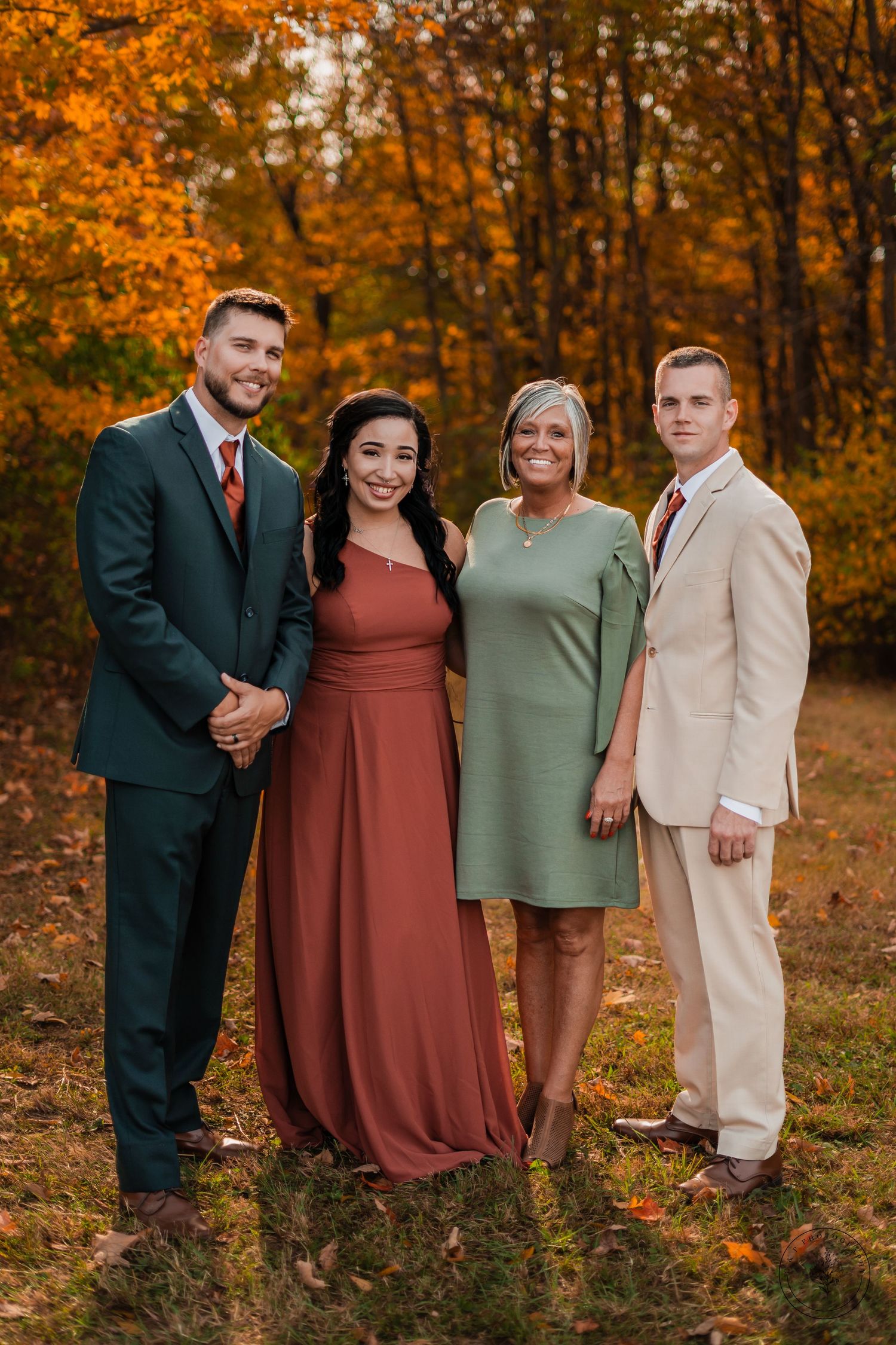 Group portrait of wedding party in formal attire against vibrant autumn foliage backdrop.
