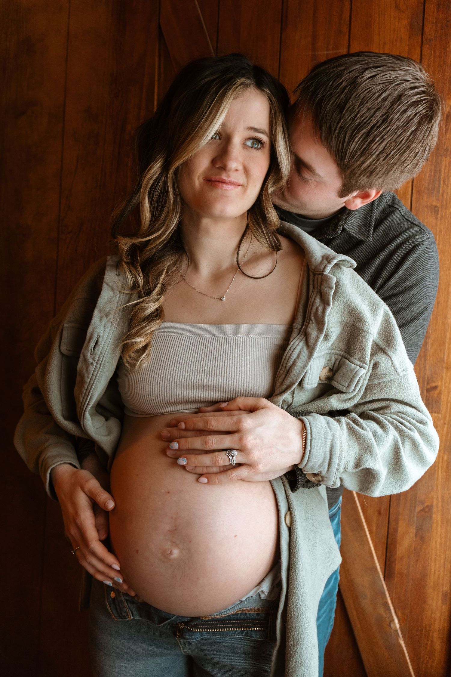 Intimate maternity photo series showing a pregnant belly against wooden paneled background.