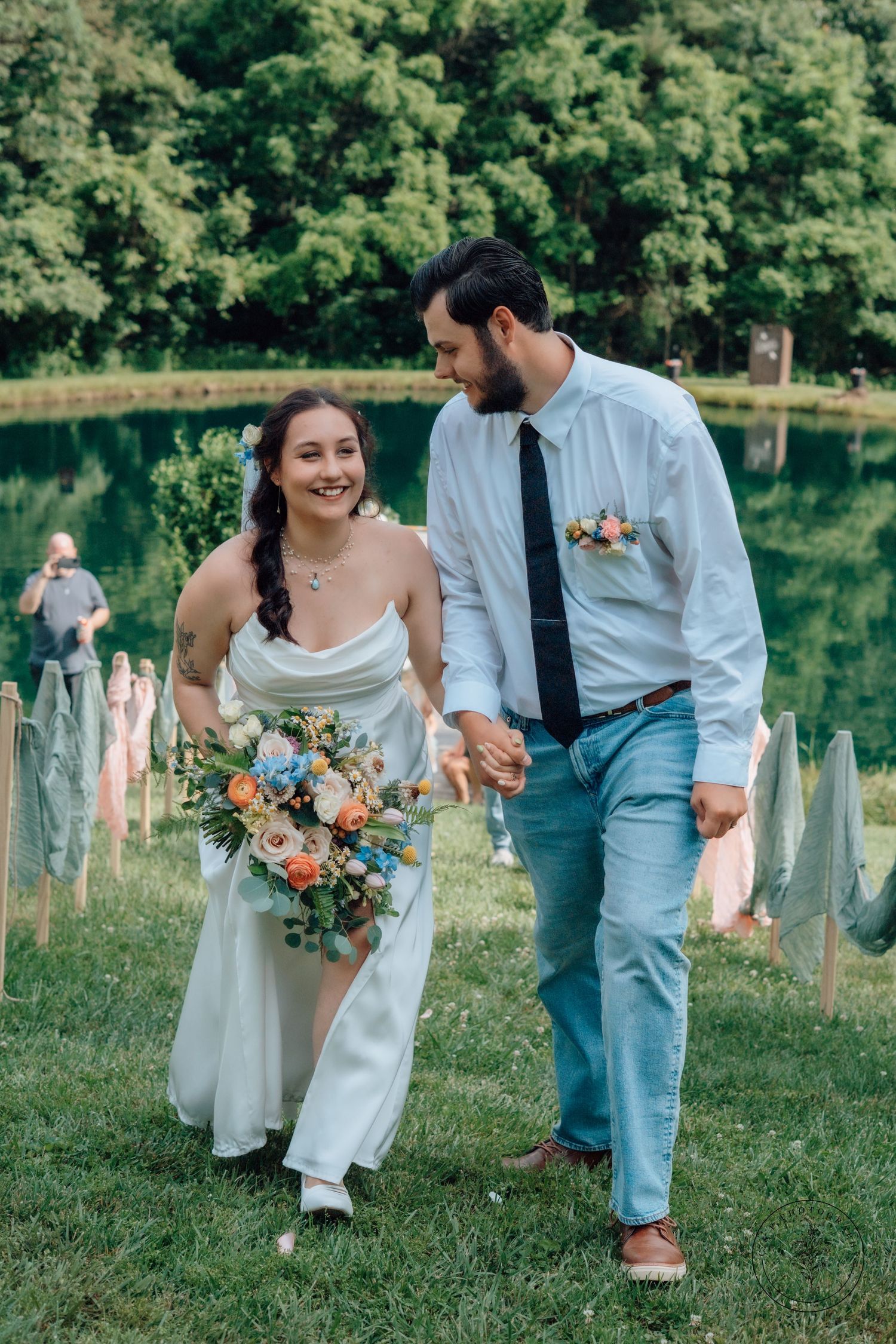 Happy newlyweds walking together by lakeside with colorful summer bouquet.