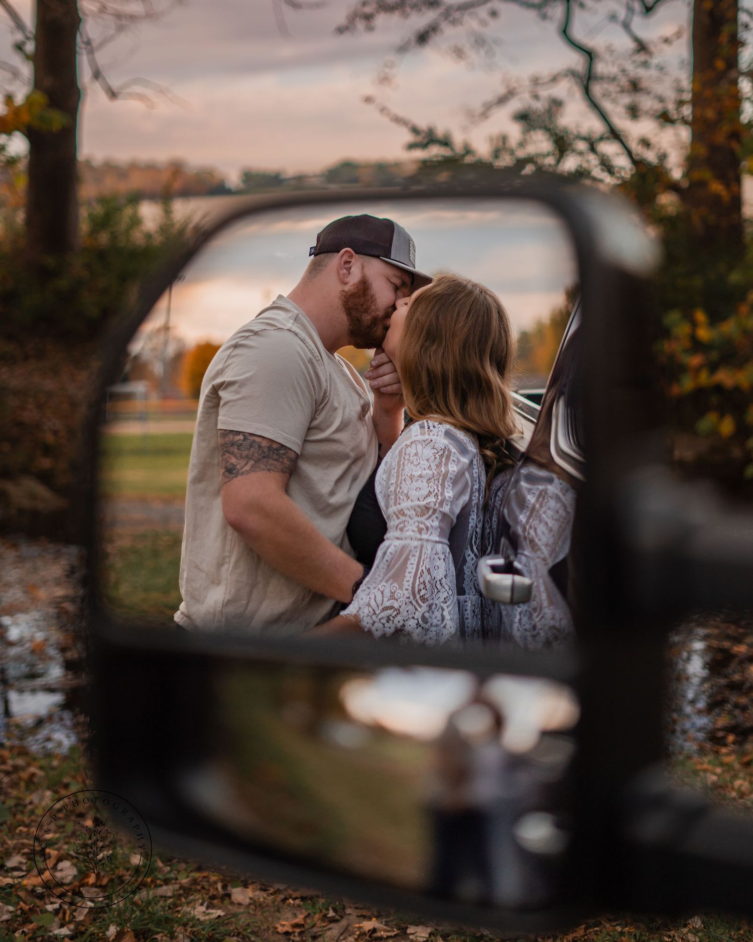 Intimate couple's portrait reflected in a car side mirror during golden hour.