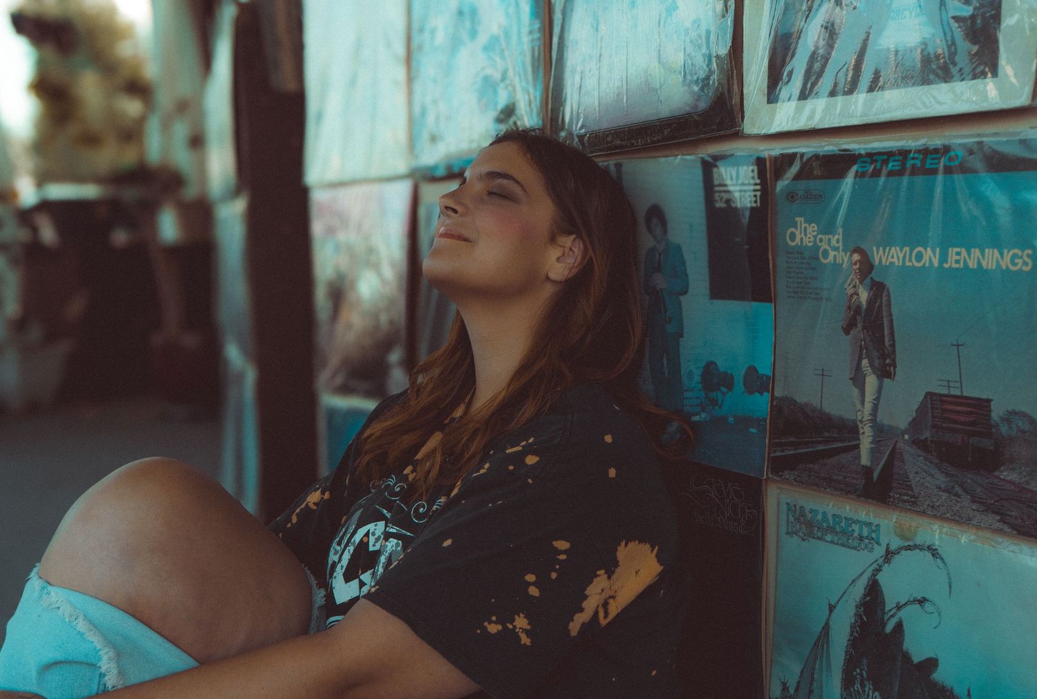 A person rests against a wall decorated with vintage posters in moody blue lighting.