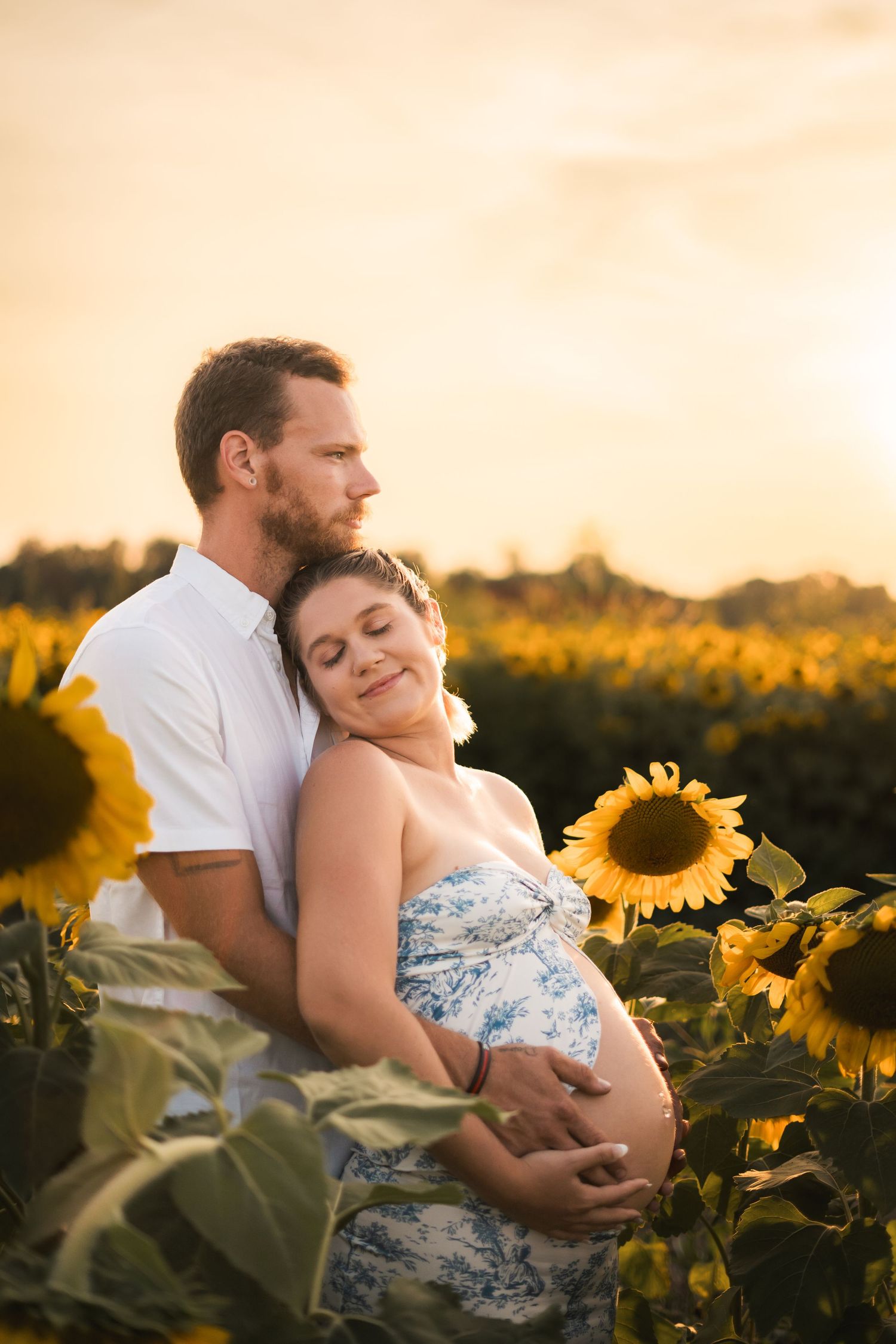 Romantic maternity photoshoot in a sunflower field at golden hour.