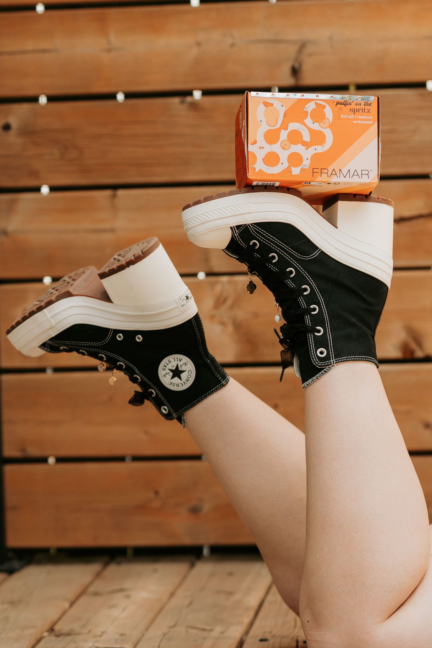 Classic black and white Converse high-top sneakers shown with orange vintage box against wooden slat background.