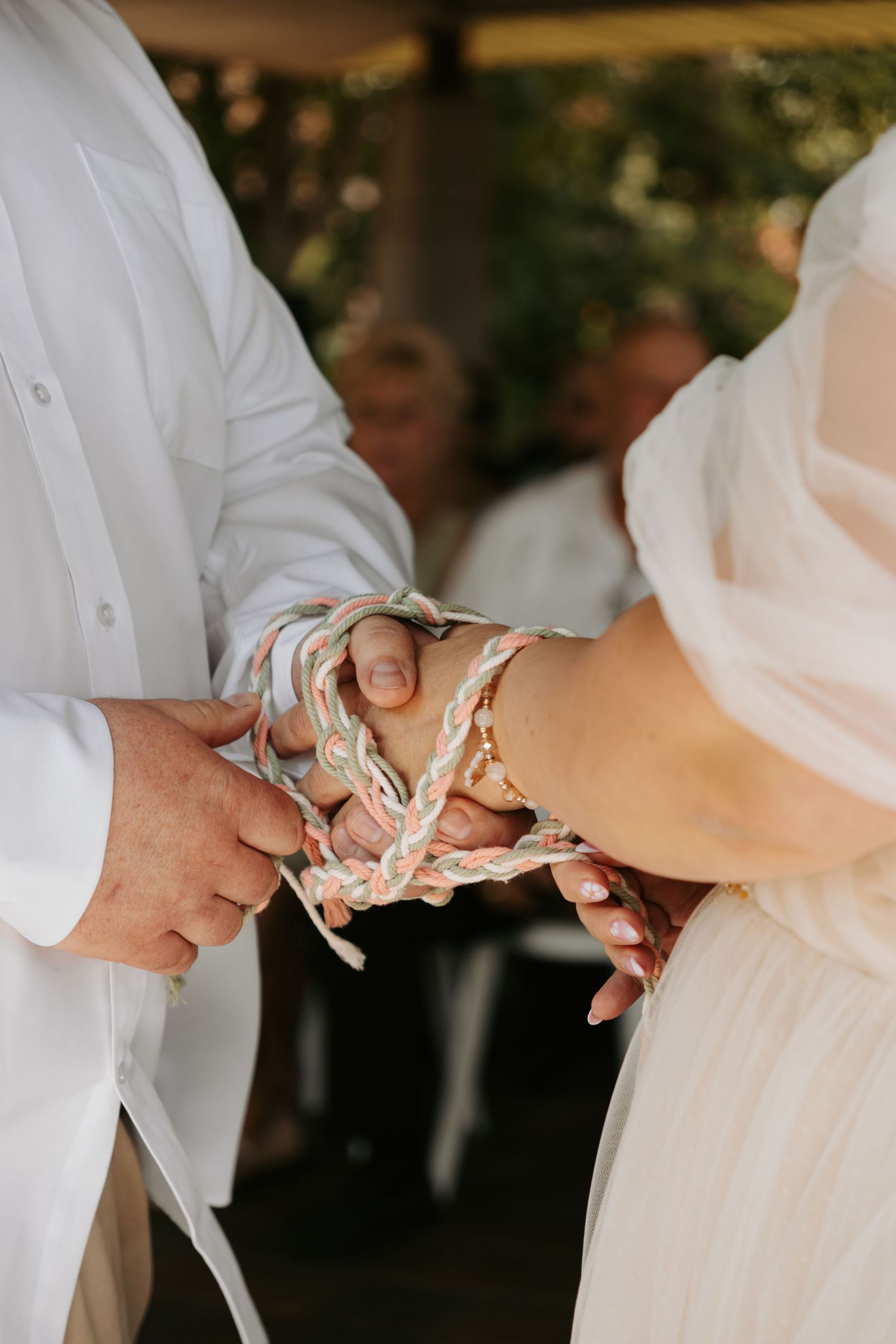 Close-up shot of couple's hands bound together in traditional handfasting ceremony during outdoor wedding ritual.